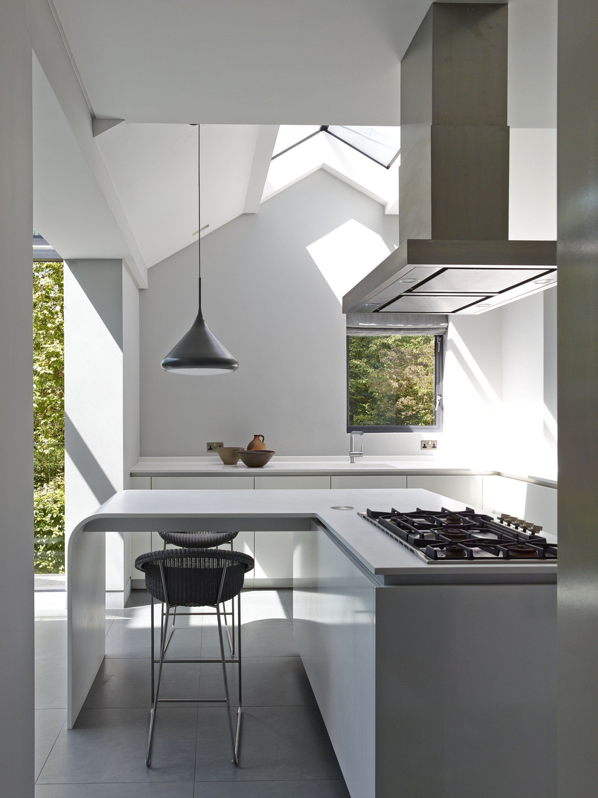 Modern white kitchen with island, black pendant light, and sunlight through windows