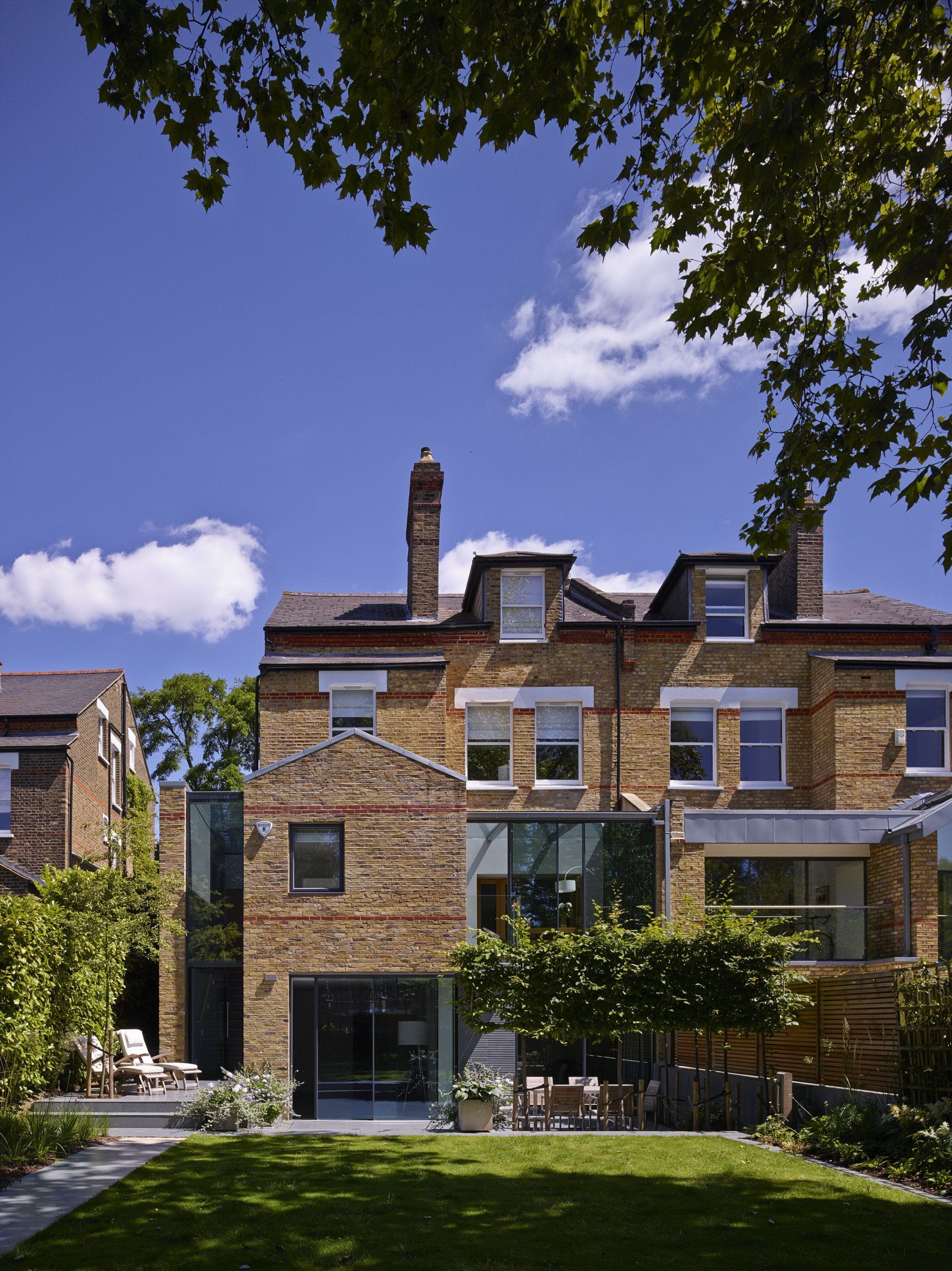 Brick townhouse with large windows and a garden under a leafy tree canopy