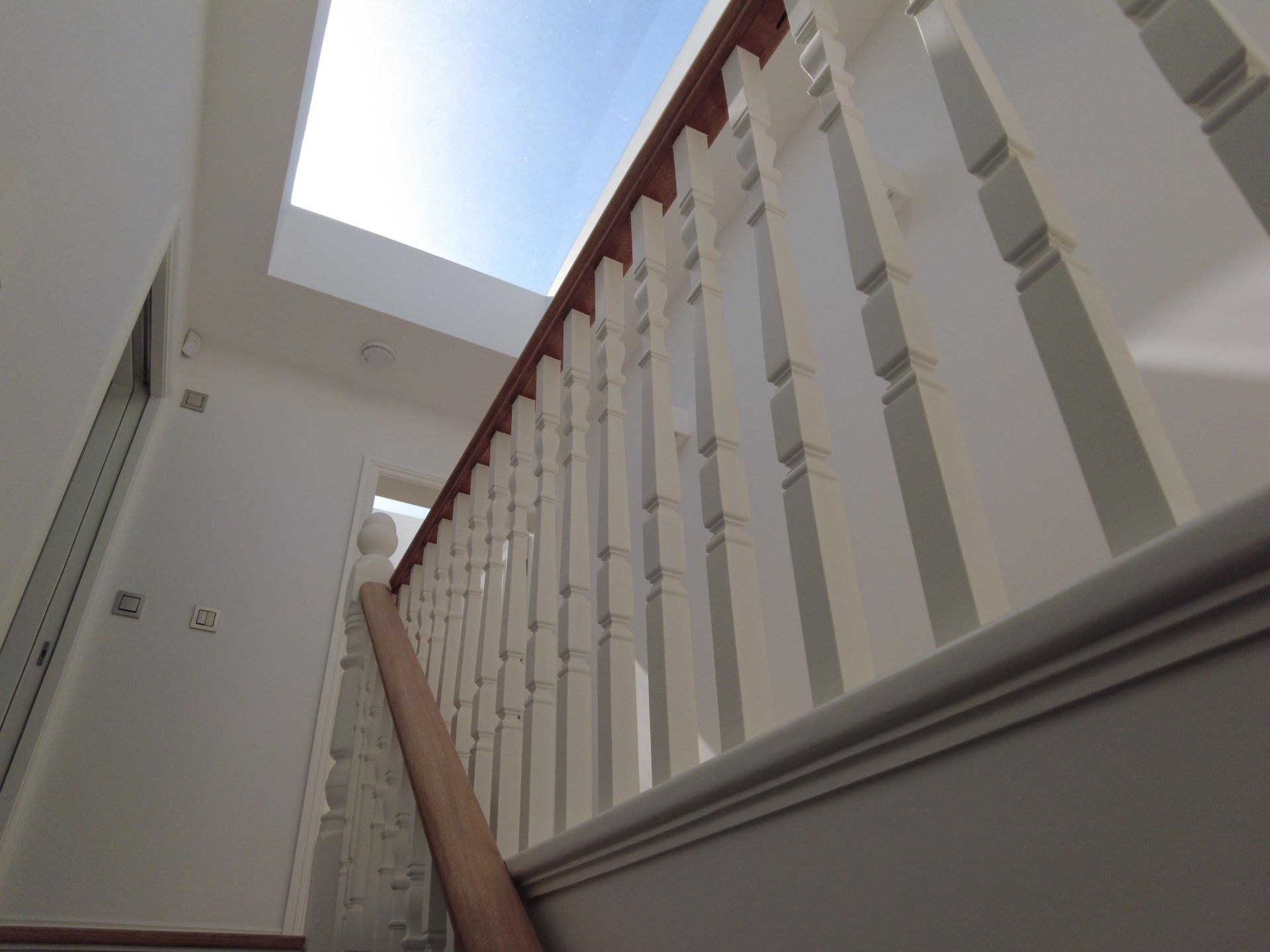 Stairwell with white railings and a skylight above, viewed from below.
