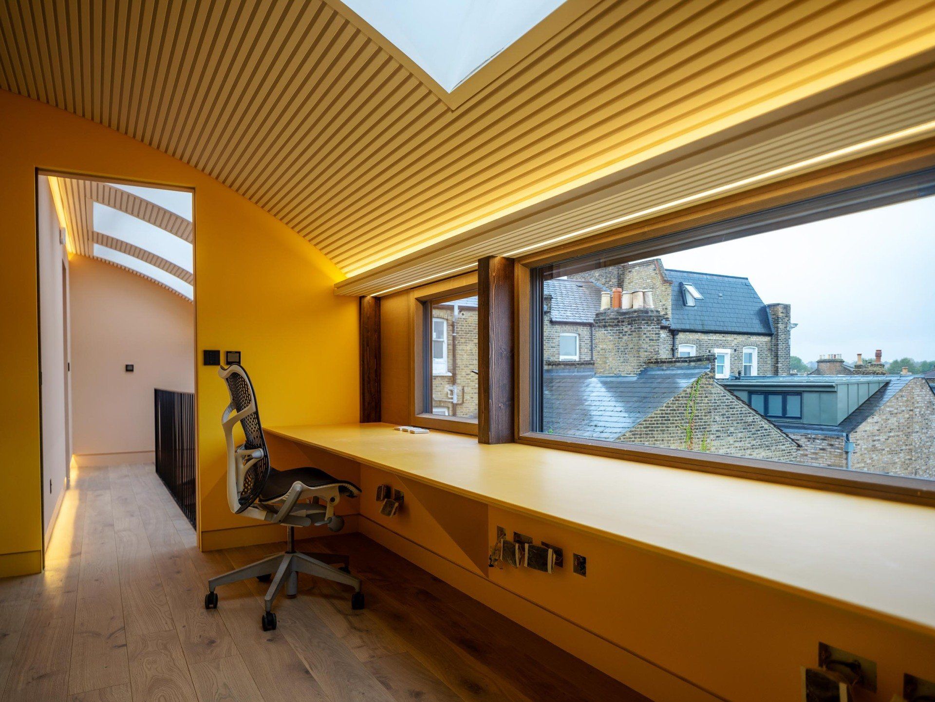Yellow attic office with long window seat, swivel chair, and city view