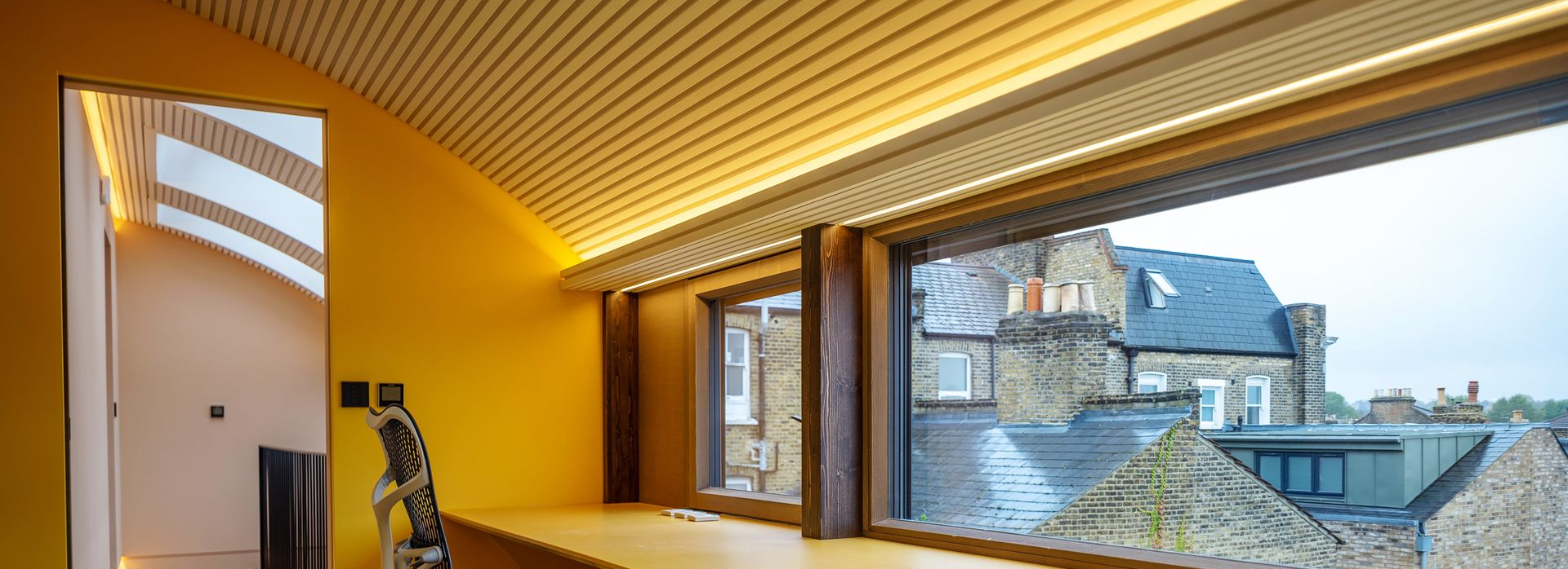 Modern interior with yellow walls, skylight ceiling, and large windows overlooking rooftops.