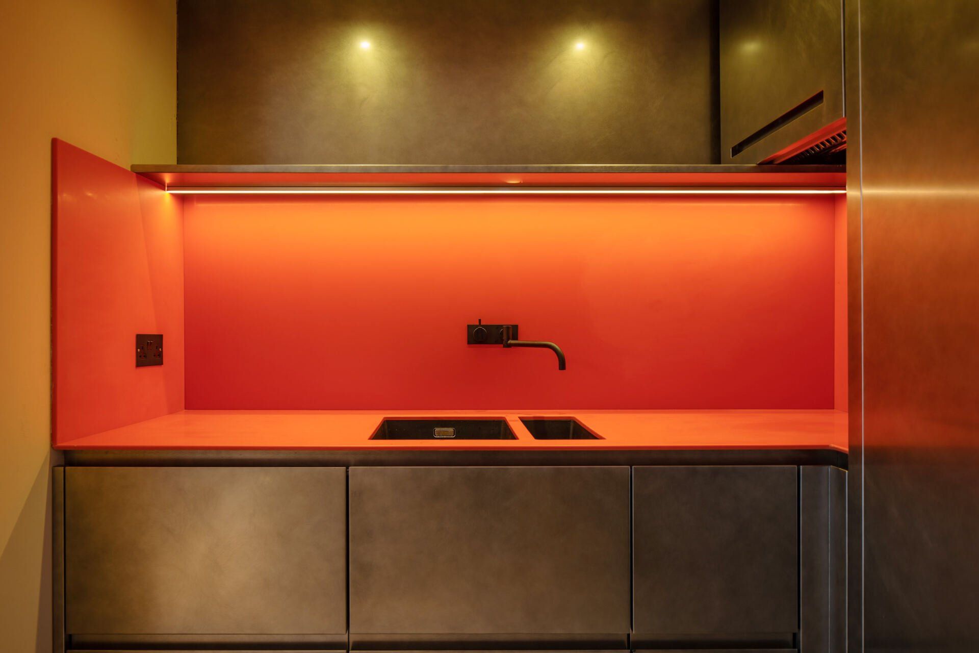 Modern kitchen nook with orange backlit backsplash, dark cabinets, and integrated sink cooktop
