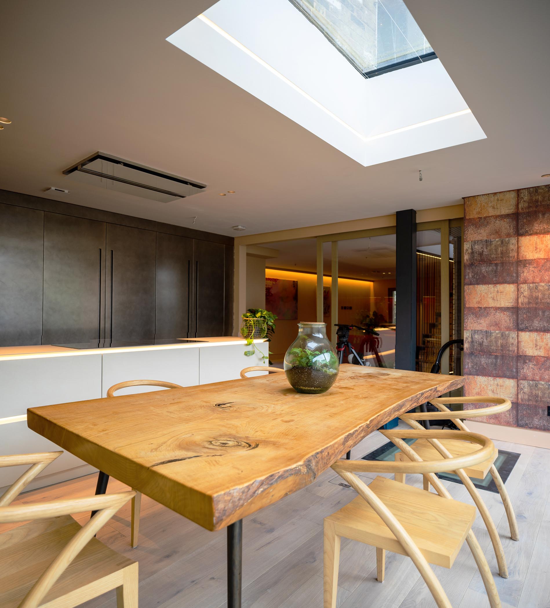 Modern dining room with a wooden table, woven chairs, skylight, and warm ambient lighting