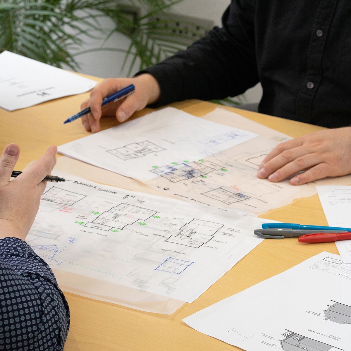 Two people review sketches and notes on paper at a desk with pens and markers.