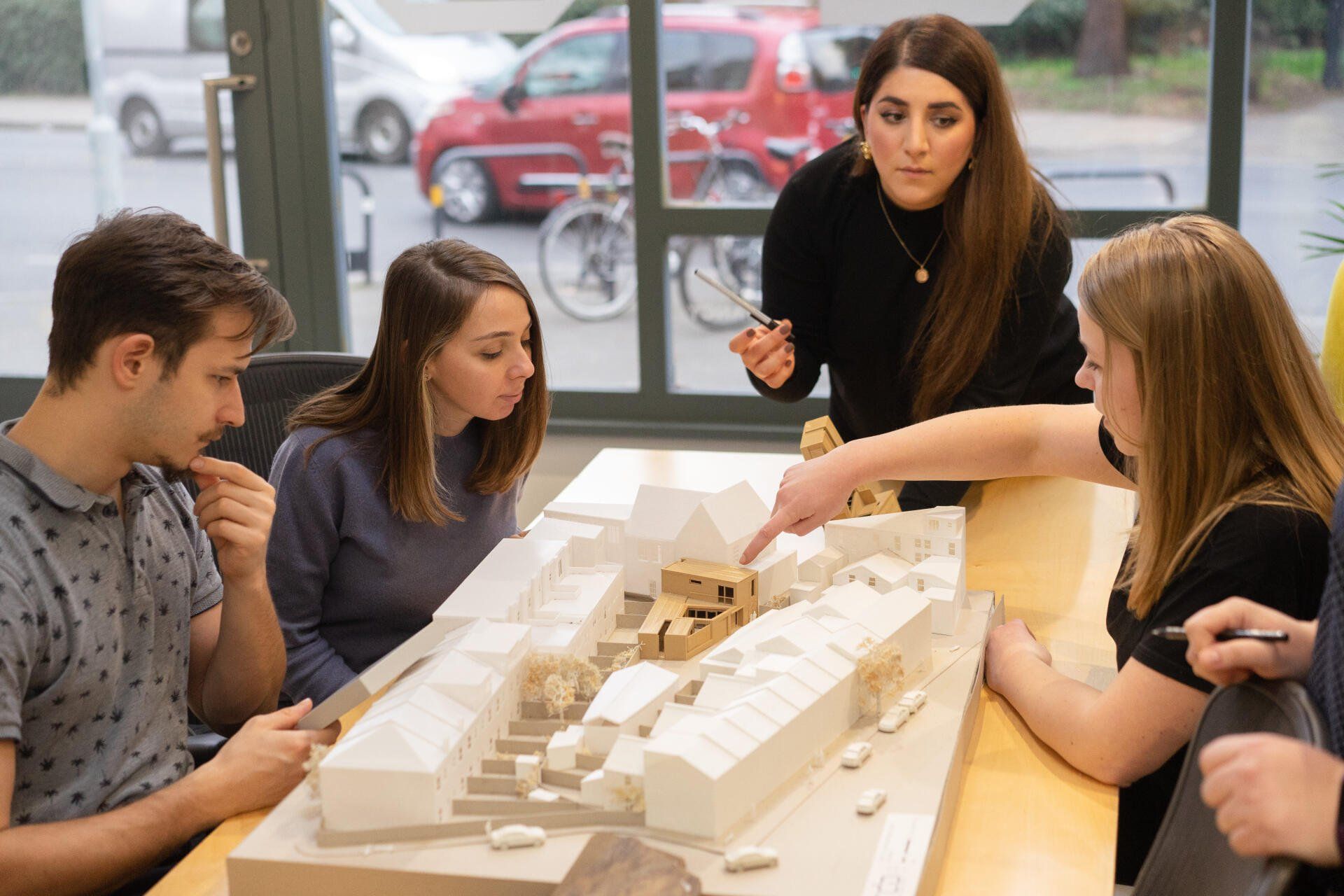 People collaborating around an architectural model at a table, discussing plans in a bright room