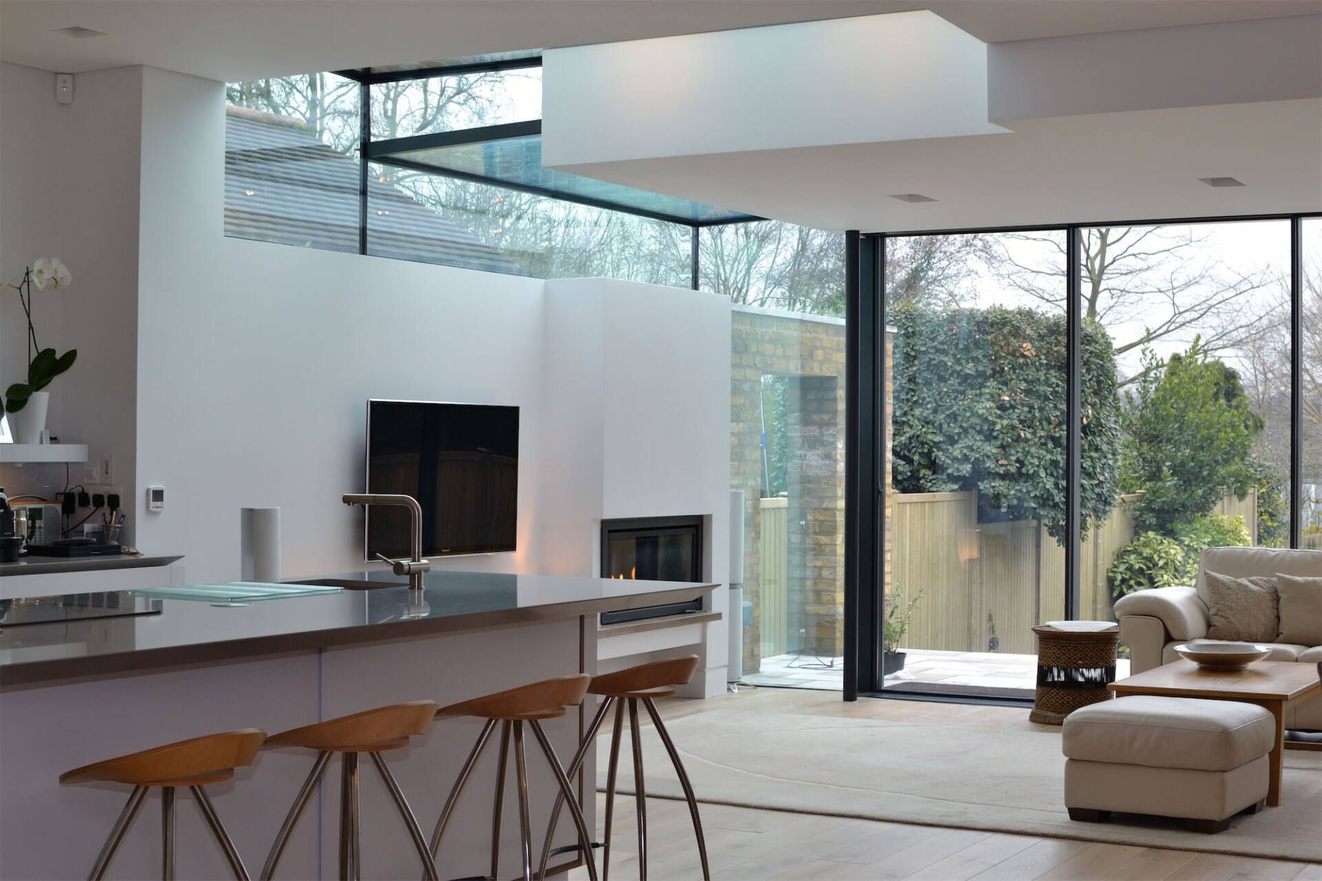 Modern open-plan living room with glass wall, kitchen island, and beige sectional seating