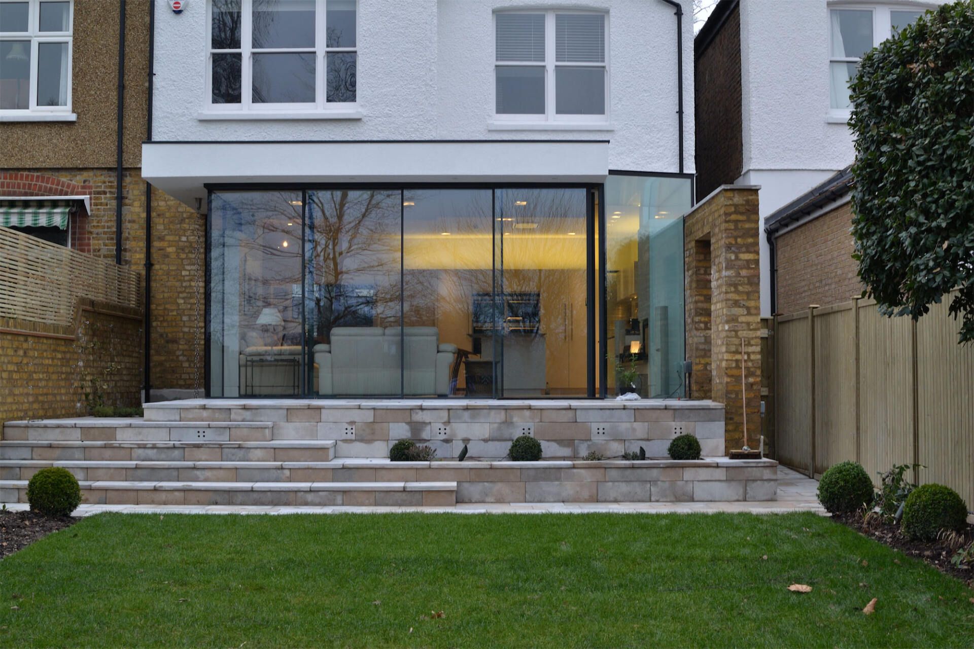 Modern house rear exterior with large glass doors, stone patio, and green lawn