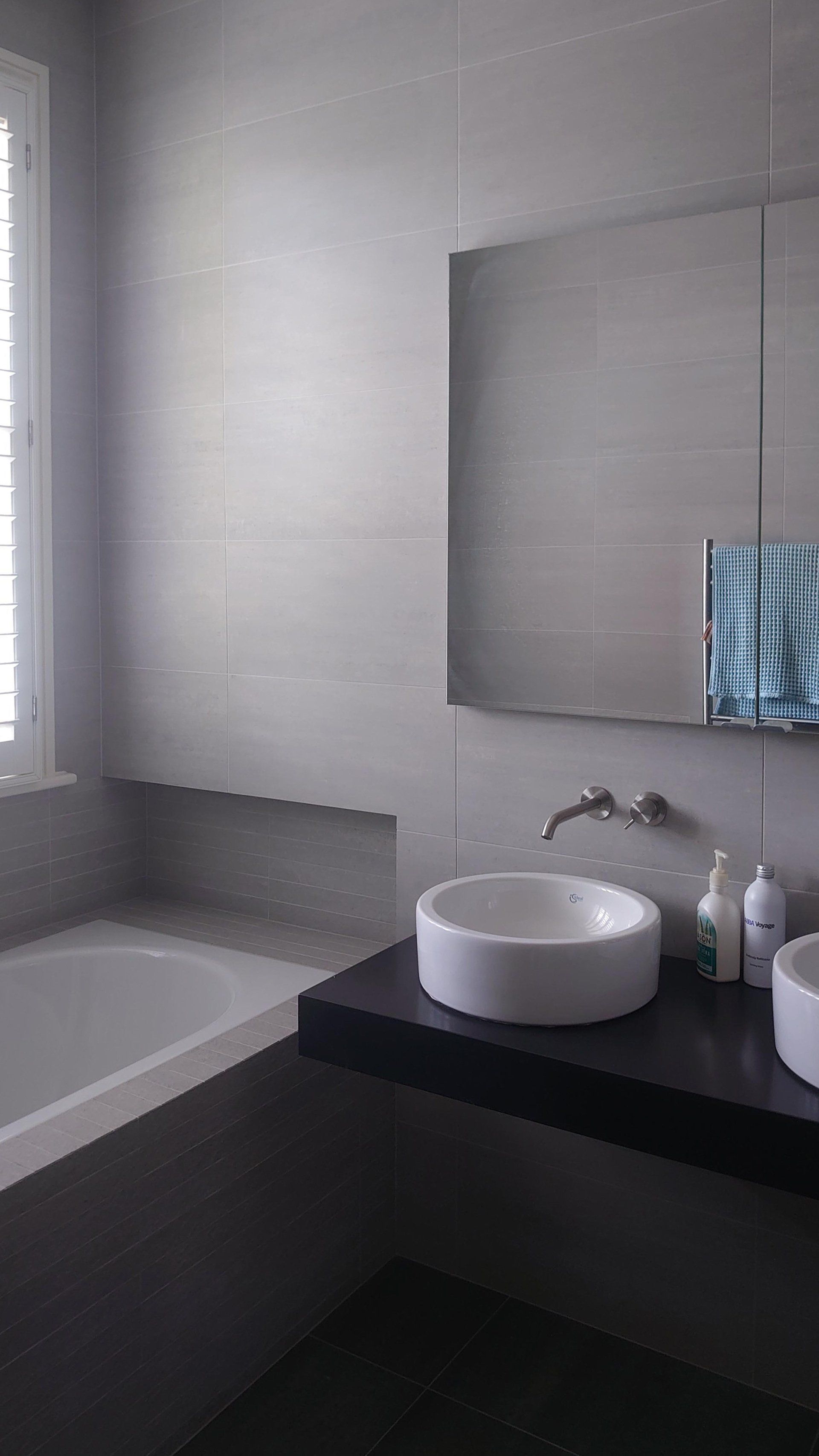 Modern bathroom with a bathtub, wall-mounted sink, mirror, and dark vanity counter