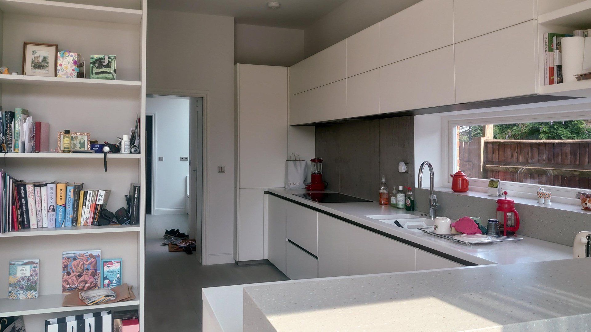 Modern kitchen with white cabinets, gray counters, open shelving, and a window above the sink
