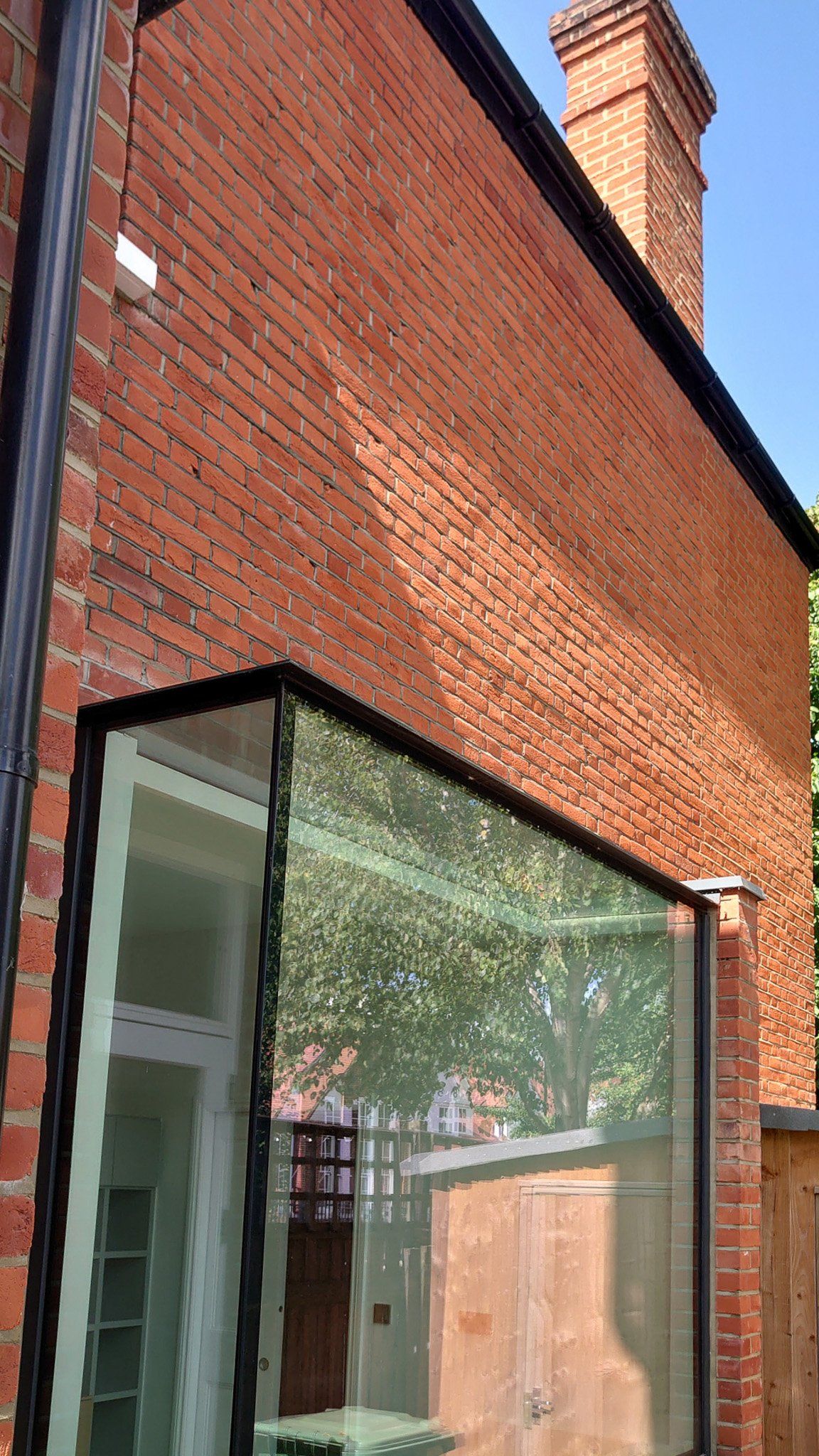 Red brick building exterior with a glass corner extension and chimney against a blue sky