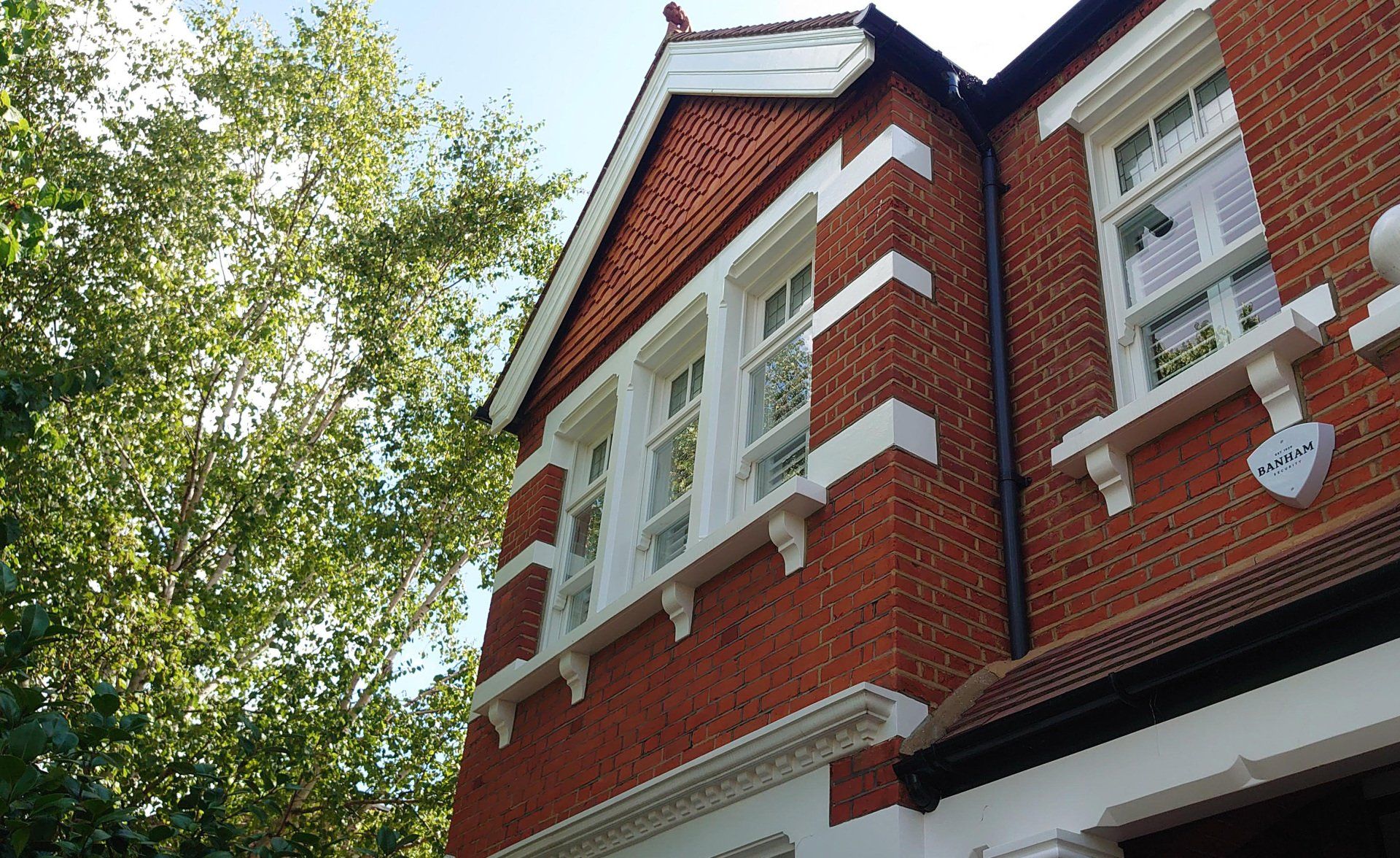Red brick house with white trim and windows viewed from below beside leafy trees