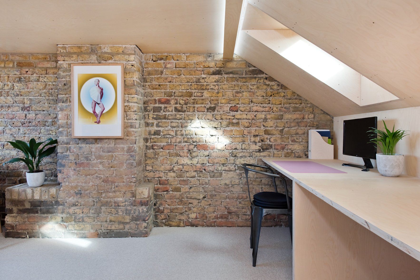 Bright office lobby with brick wall, abstract art, plants, and a reception desk under skylight