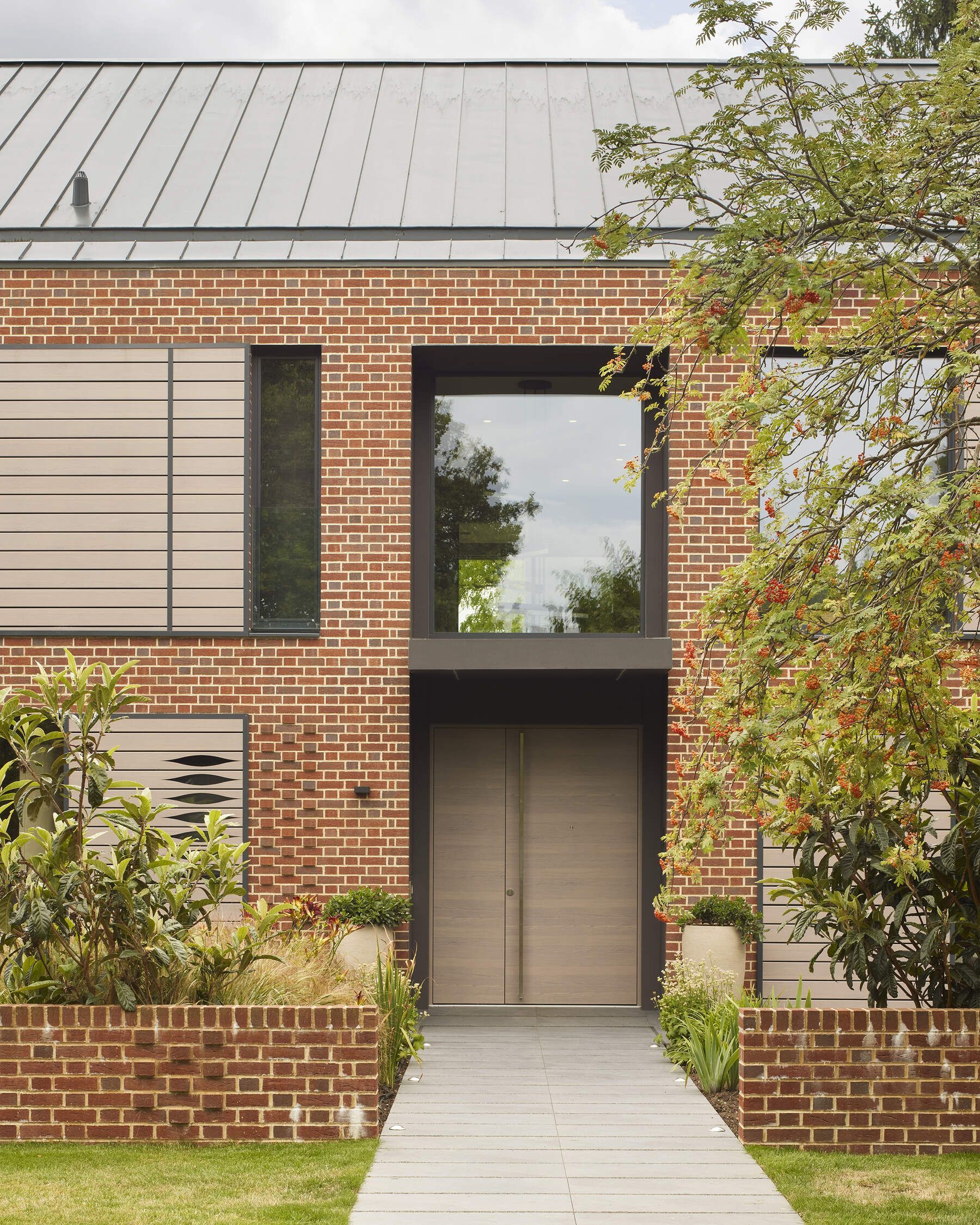 Modern brick townhouse entrance with a central wooden door, large window, and landscaped front walkway.
