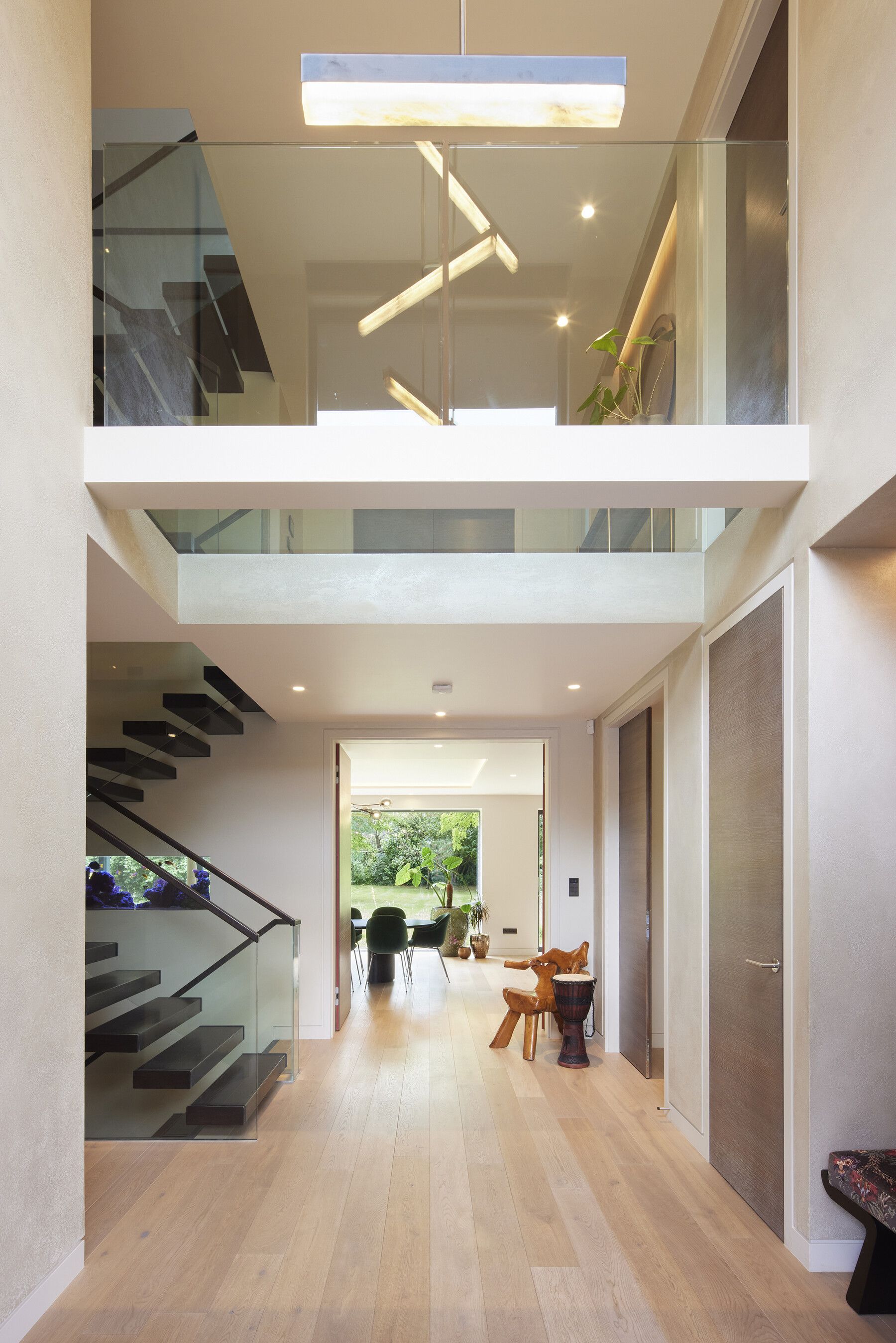 Modern open-concept hallway with wood floors, glass stairs, skylights, and dining area beyond