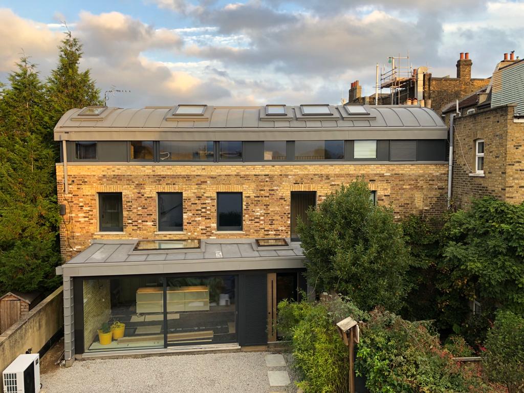 Modern brick house with rooftop skylights, large windows, and a glass patio facing a leafy garden