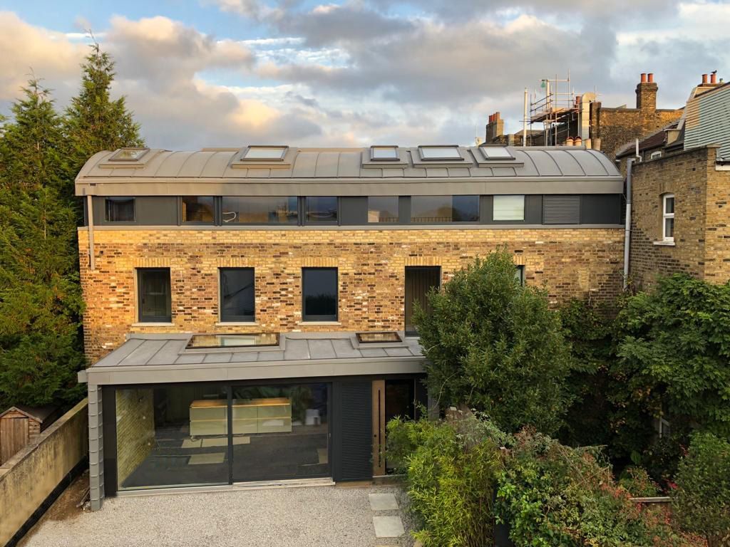 Modern brick house with rooftop skylights, large windows, and a covered front entrance surrounded by trees
