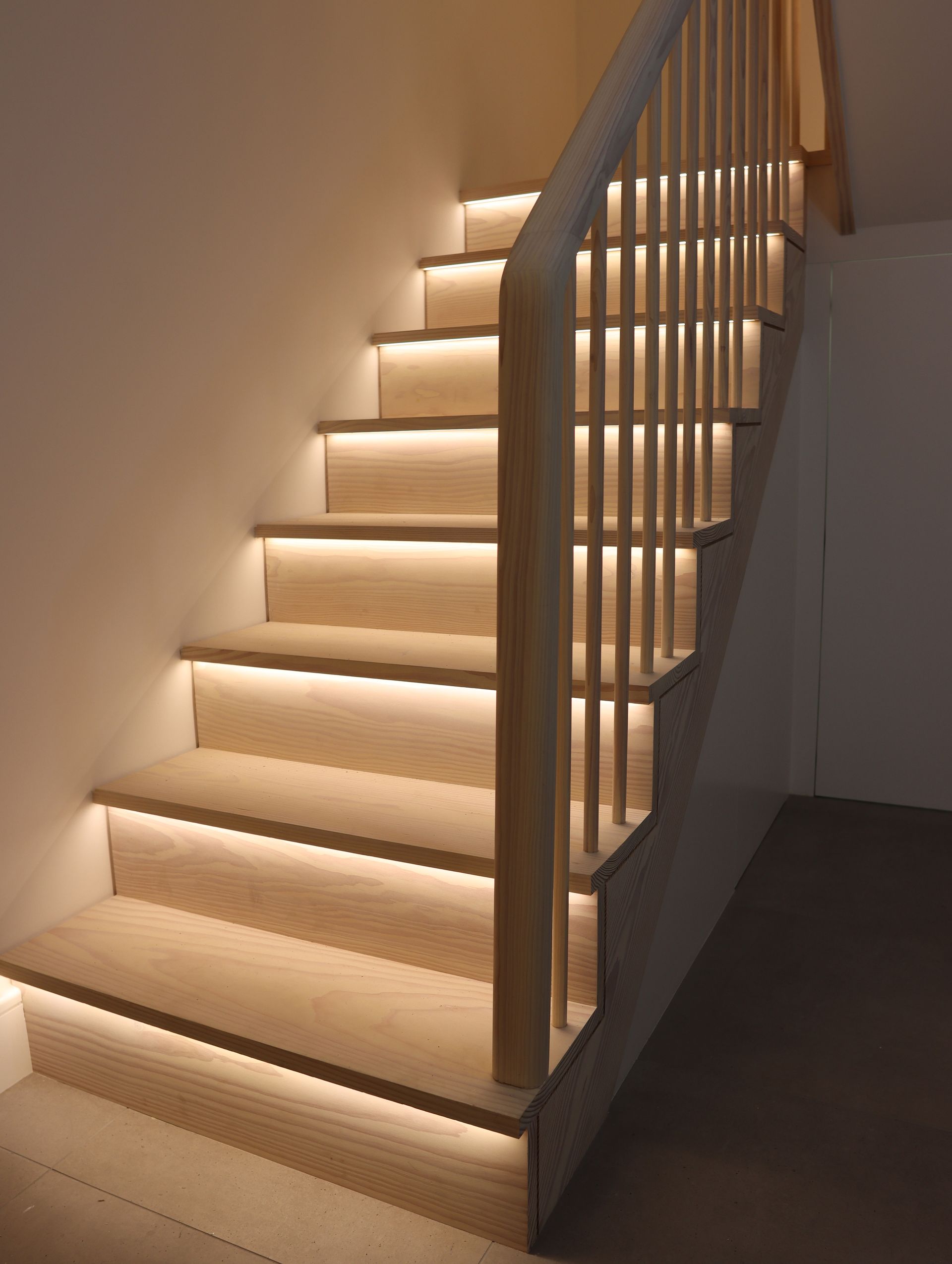 Modern staircase with black vertical railings, white walls, and a small indoor planter below.