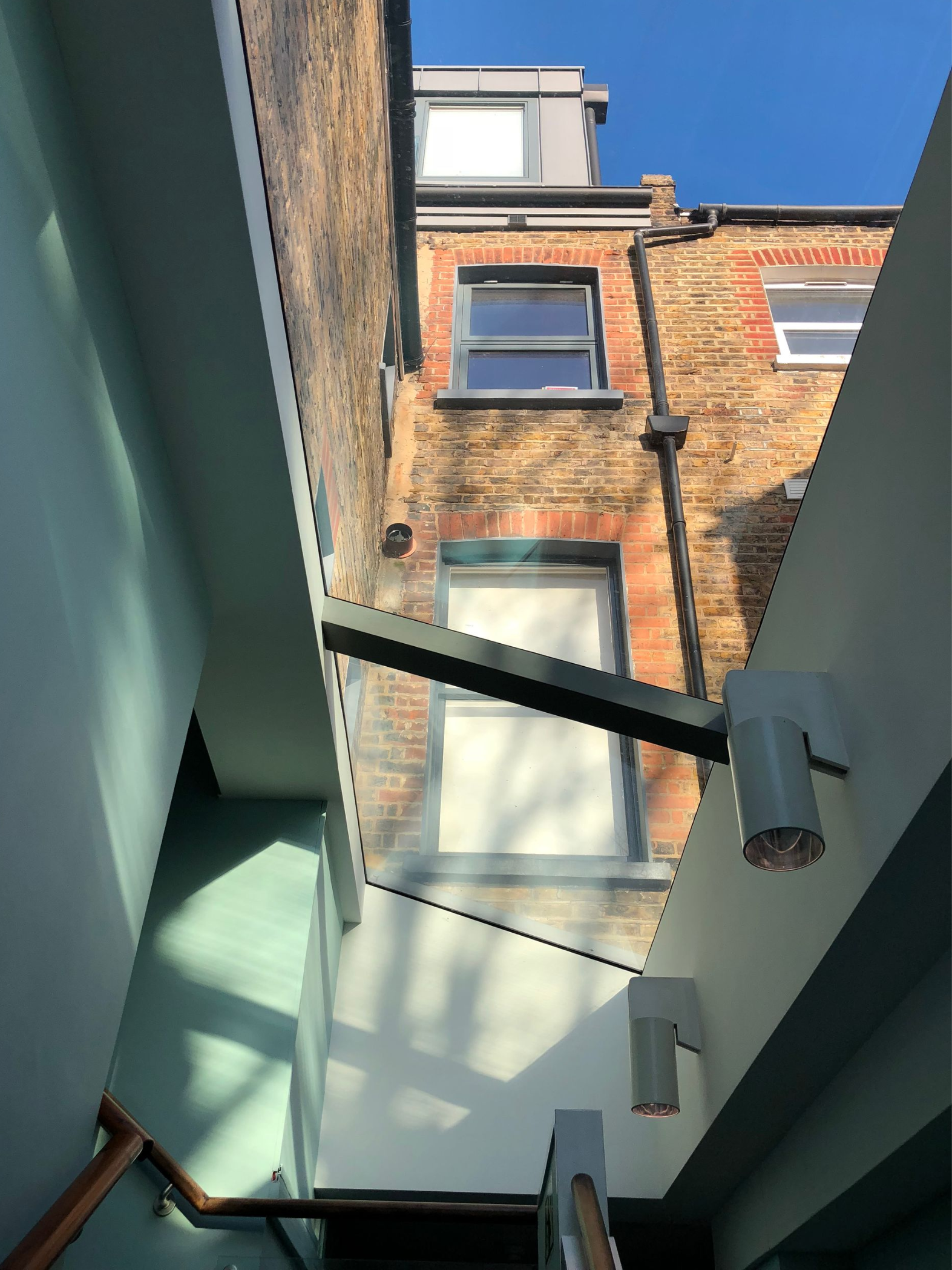 Narrow glass-roofed courtyard between pale green walls, looking up at brick apartment buildings and blue sky.