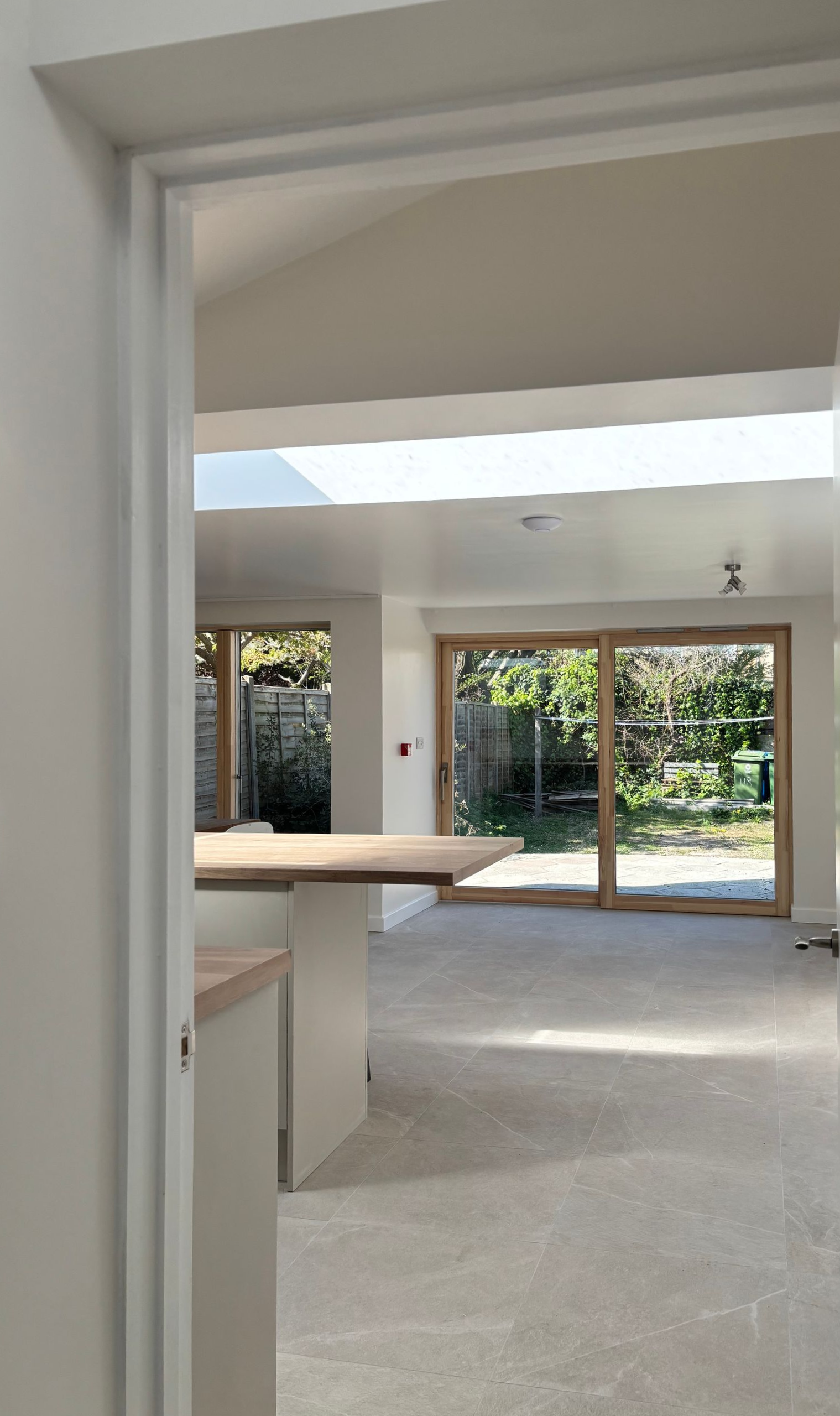 Bright empty living space with beige carpet, white walls, and large sliding glass doors opening to a garden.