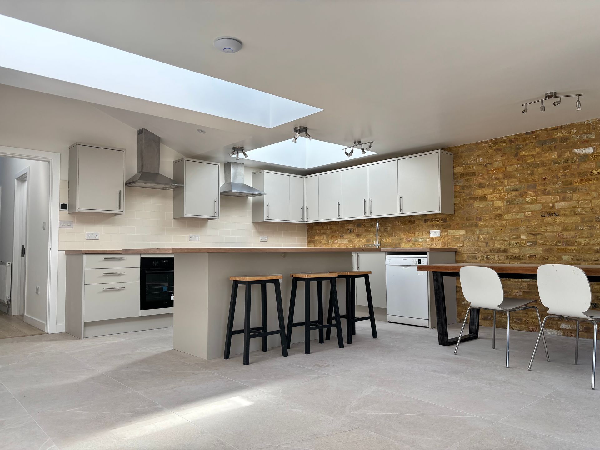 Modern white kitchen with island stools, stone accent wall, and bright skylight