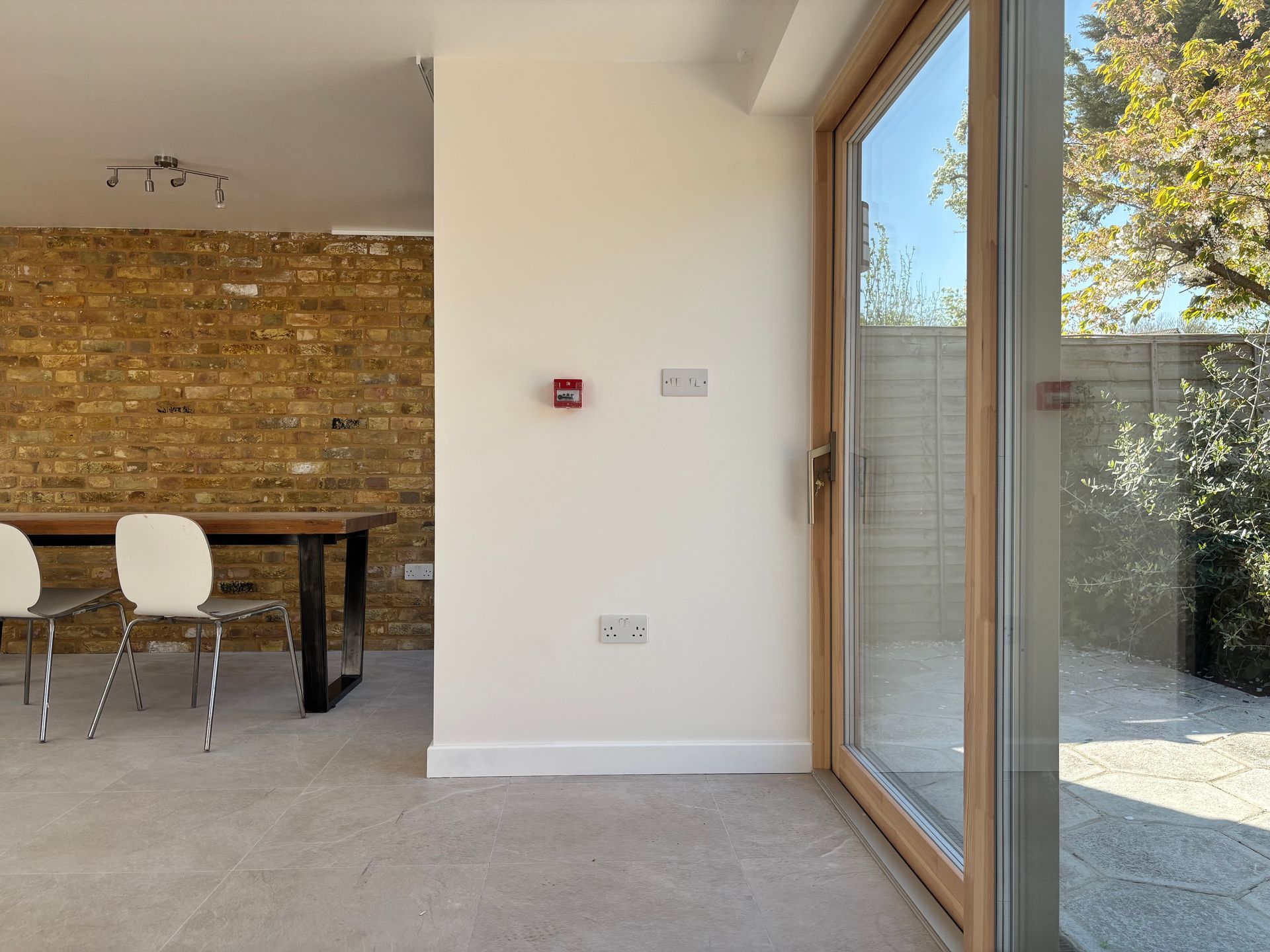 Modern dining room with a stone wall, black table, white chairs, and a large glass door to the patio.