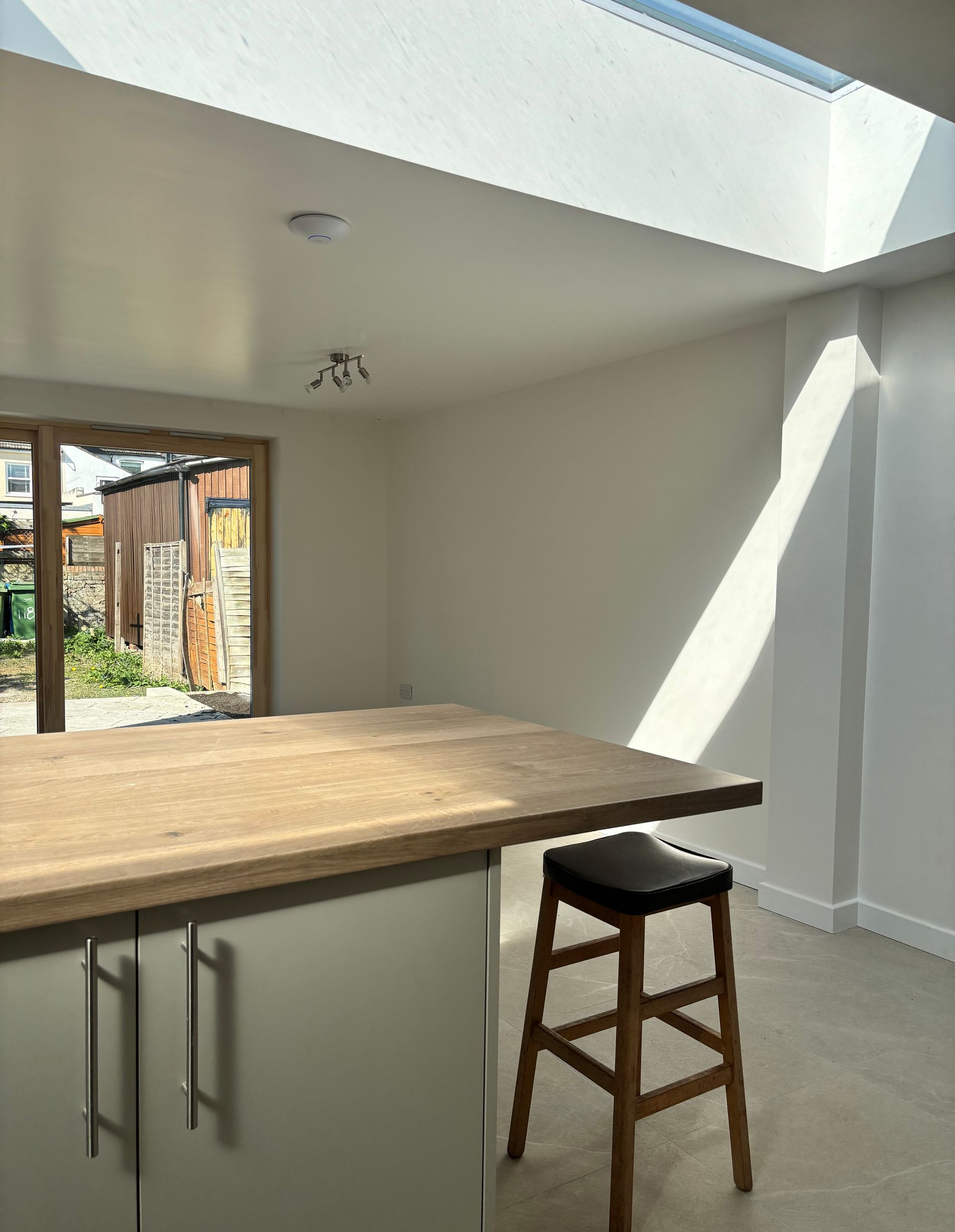 Bright kitchen with wooden island, stool, skylight, and open doorway to a yard.