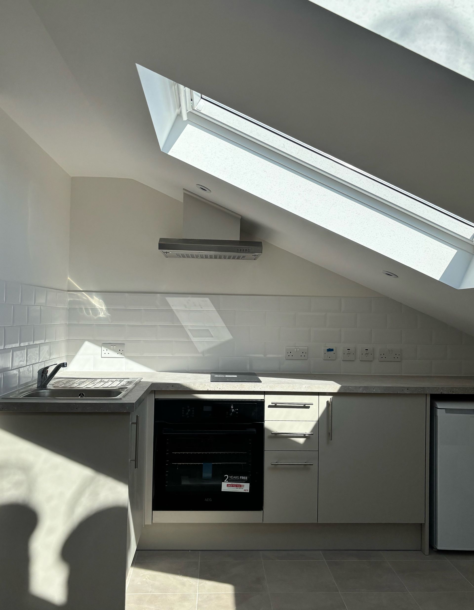 Bright kitchen with slanted skylight, white cabinets, black oven, and a small window on the right.