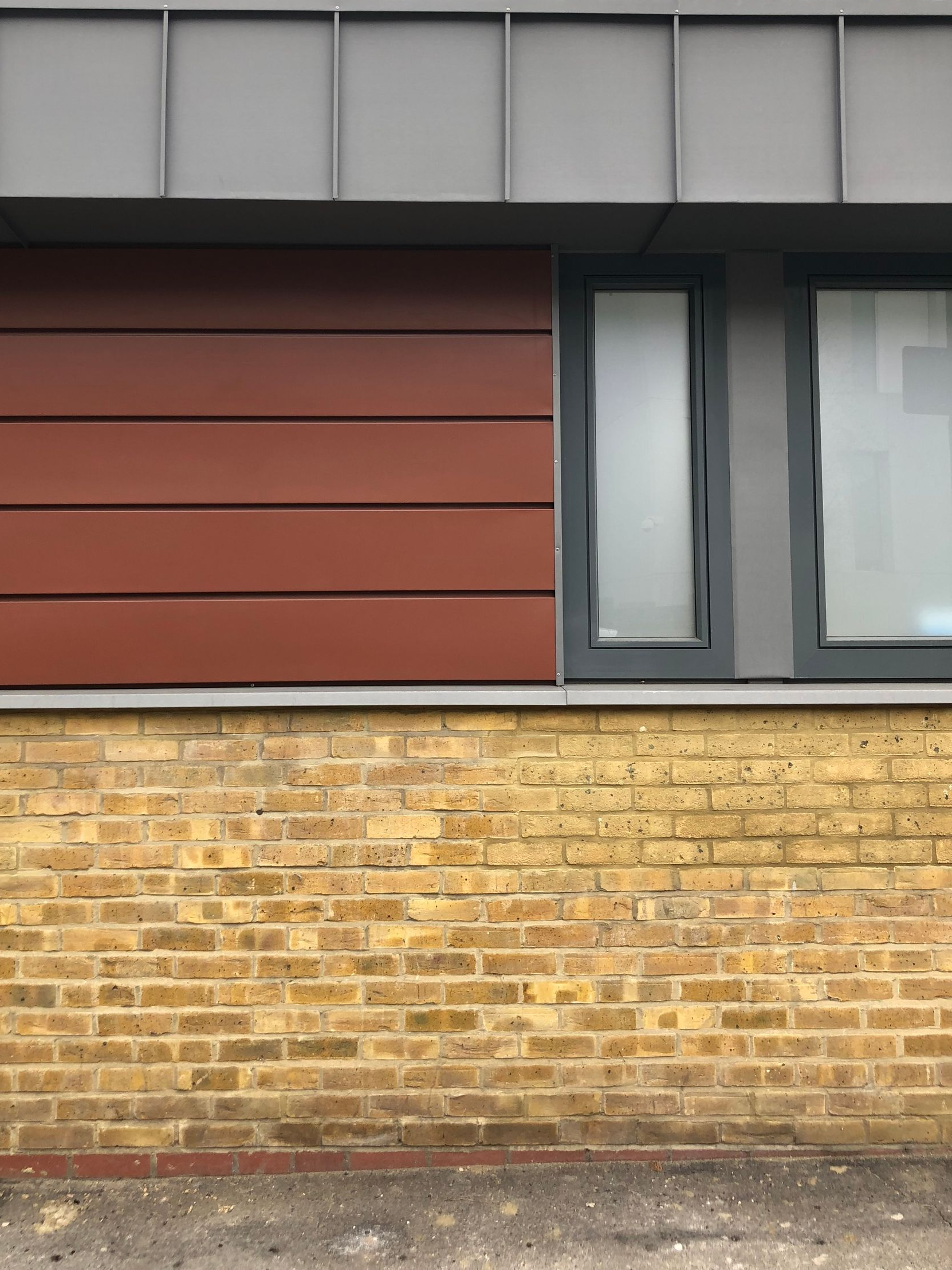 Exterior wall with brick lower half, red panels, and a gray-framed window