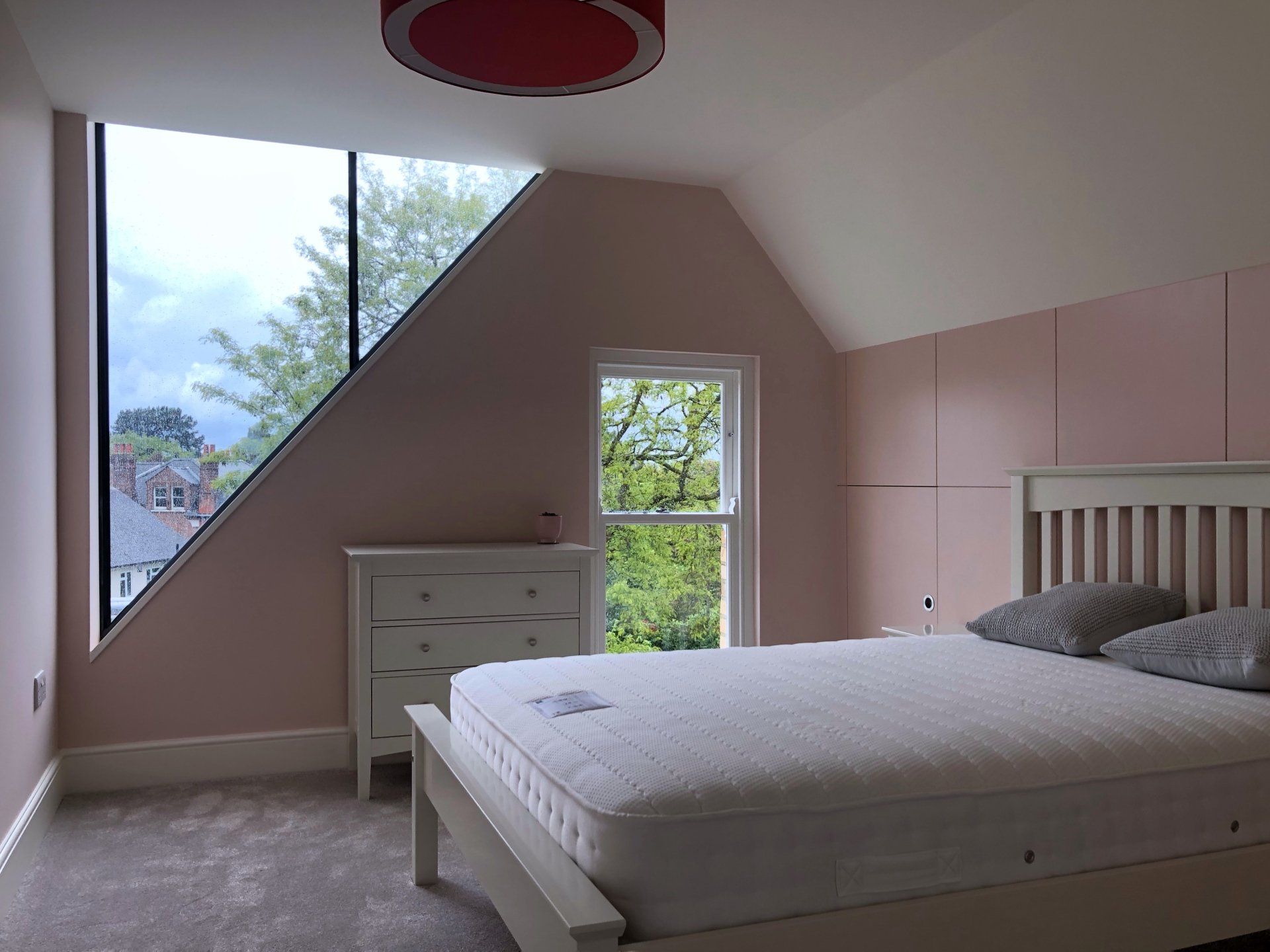 Bright bedroom with slanted ceiling, pink walls, large window, and white bed