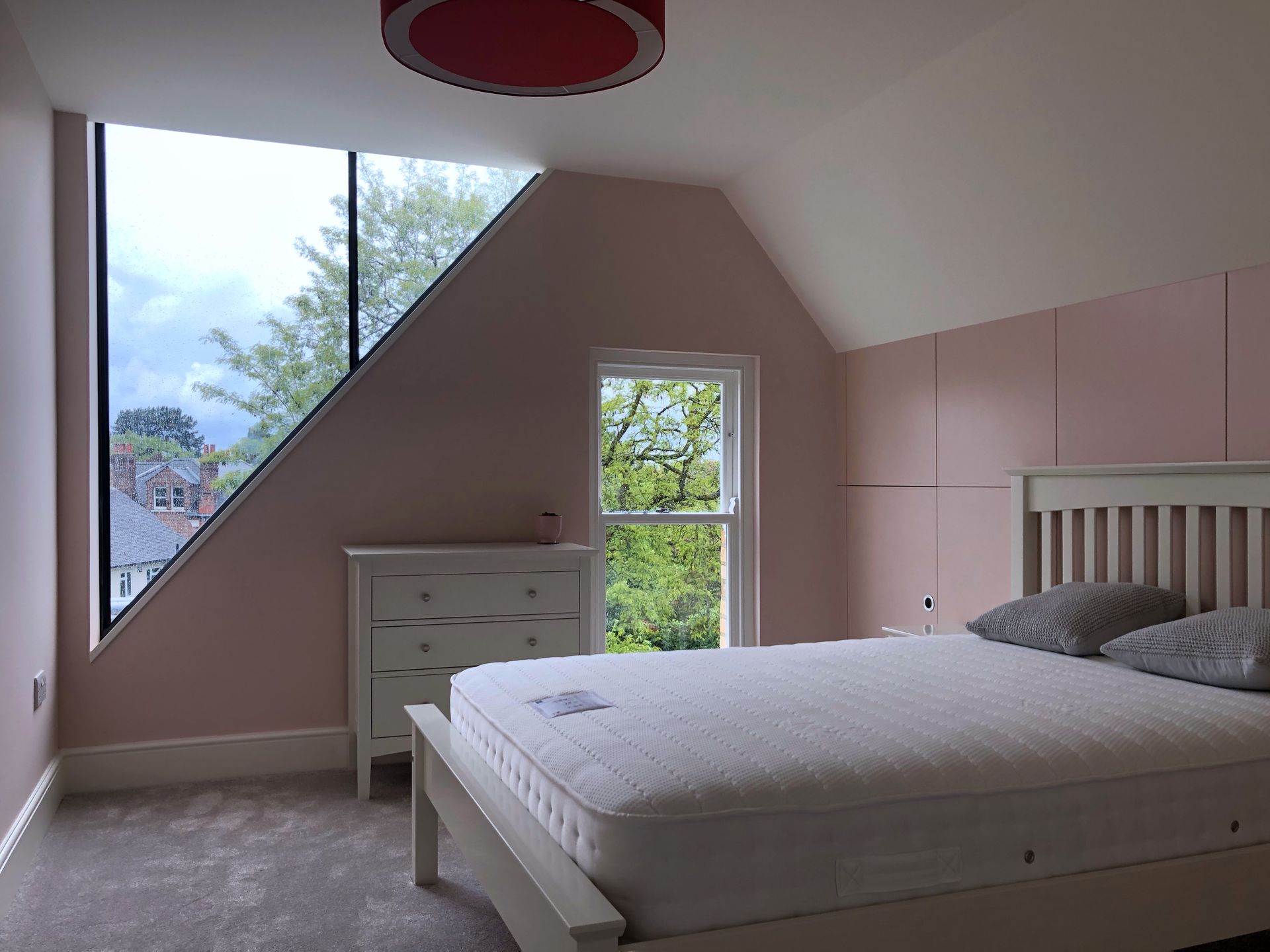 Bedroom with slanted ceiling, large triangular window, pink walls, and a bed with gray bedding.