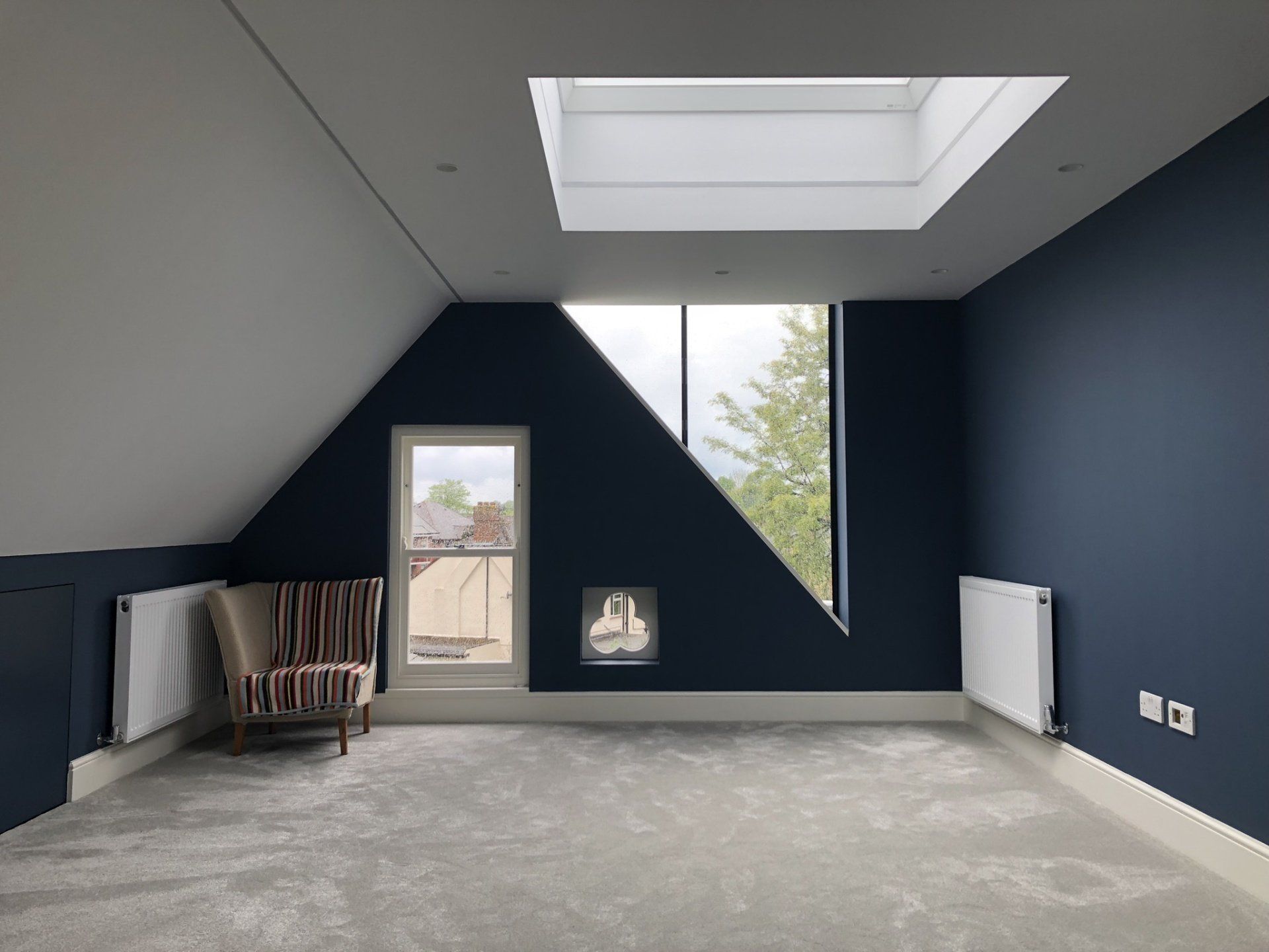 Empty blue attic room with skylight, slanted ceiling, window, radiator, and paint cans on the floor