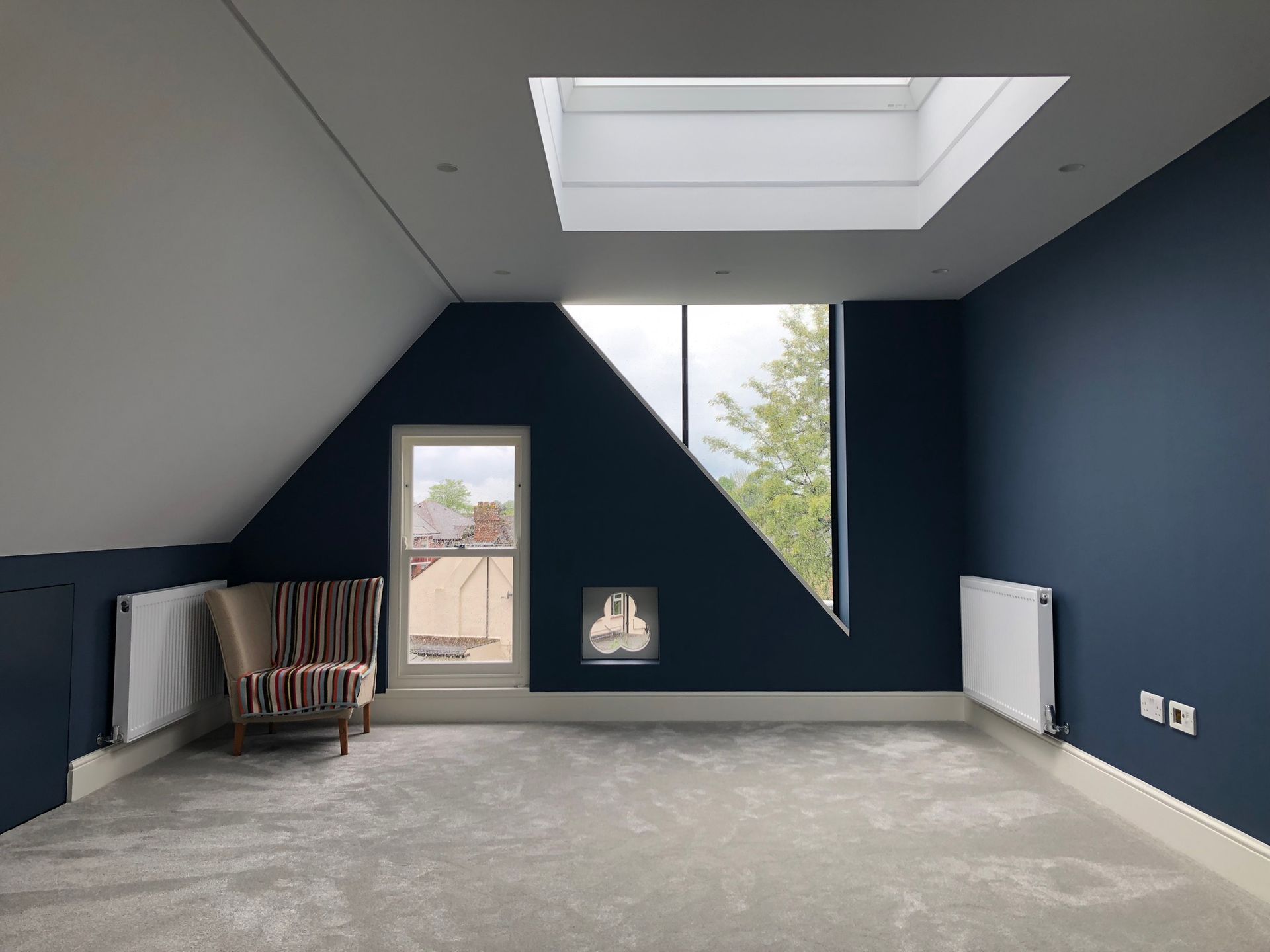 Empty attic room with blue walls, skylight, radiator, and a windowed door.
