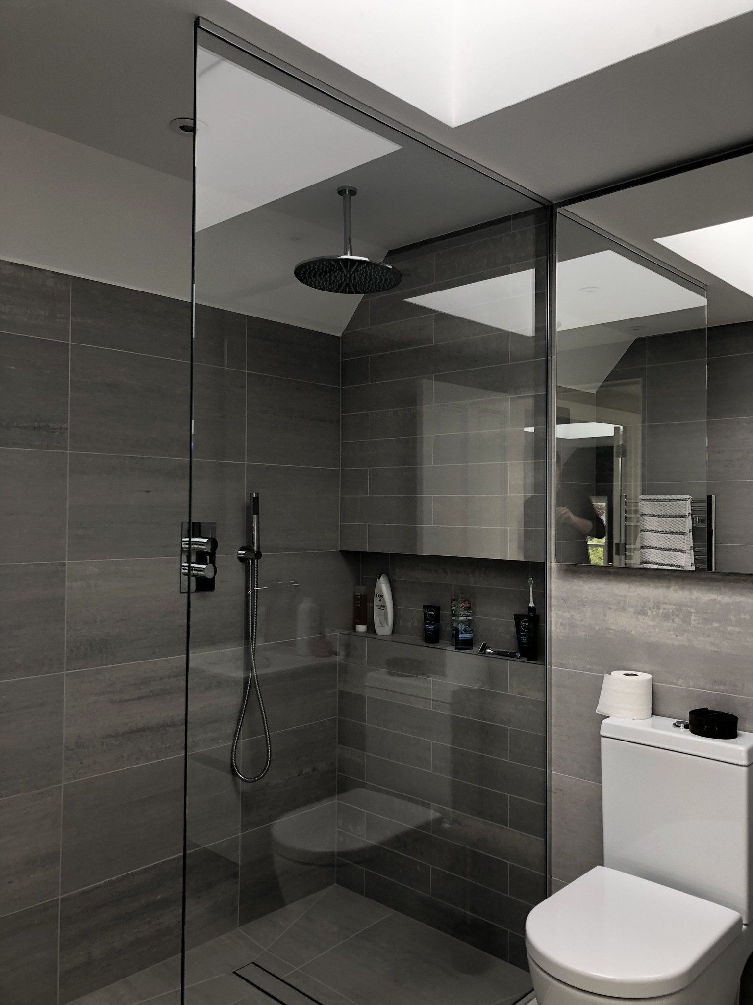 Modern bathroom with a glass shower enclosure and a white toilet beside gray tiled walls.