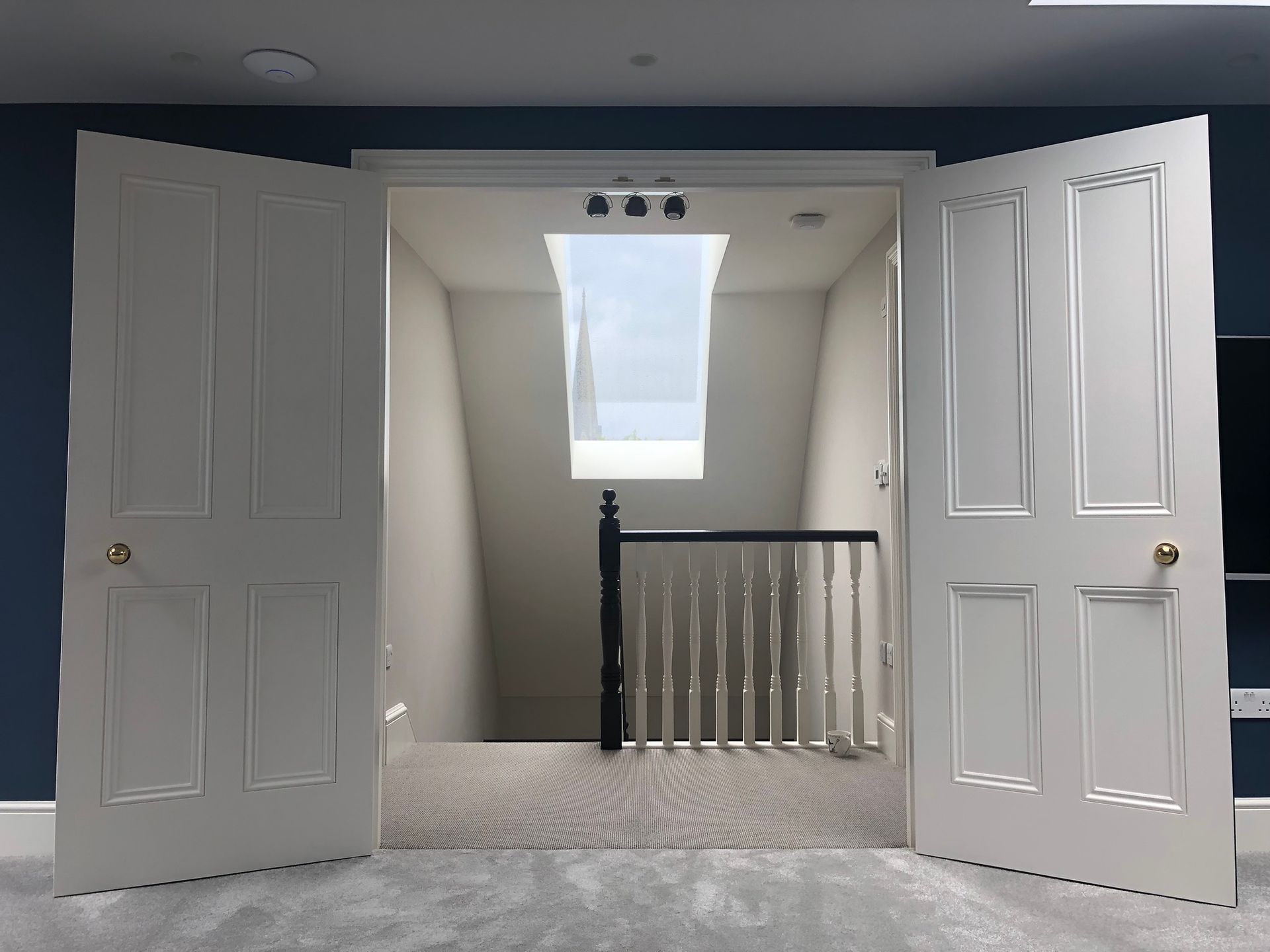 Open white double doors framing a hallway with a skylight and staircase railing beyond.