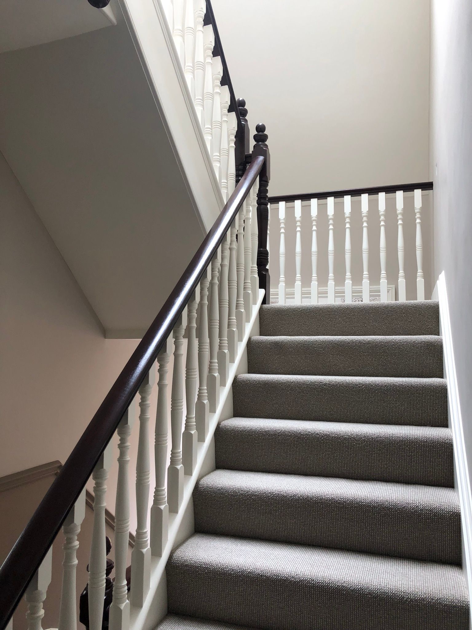 Carpeted indoor staircase with white balusters and dark handrail, viewed from the bottom up.