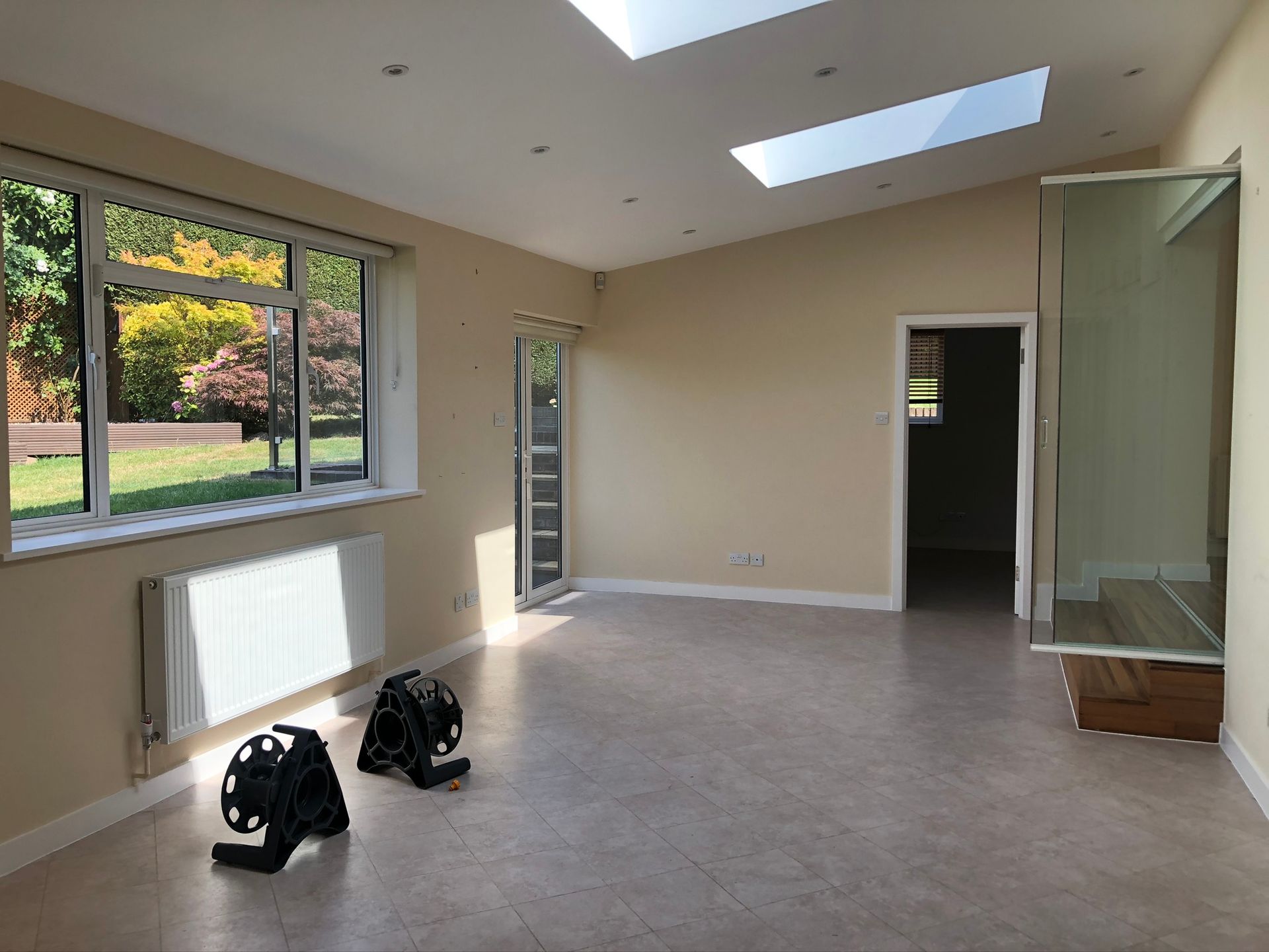 Empty modern room with large windows, skylights, and two black fans on the floor
