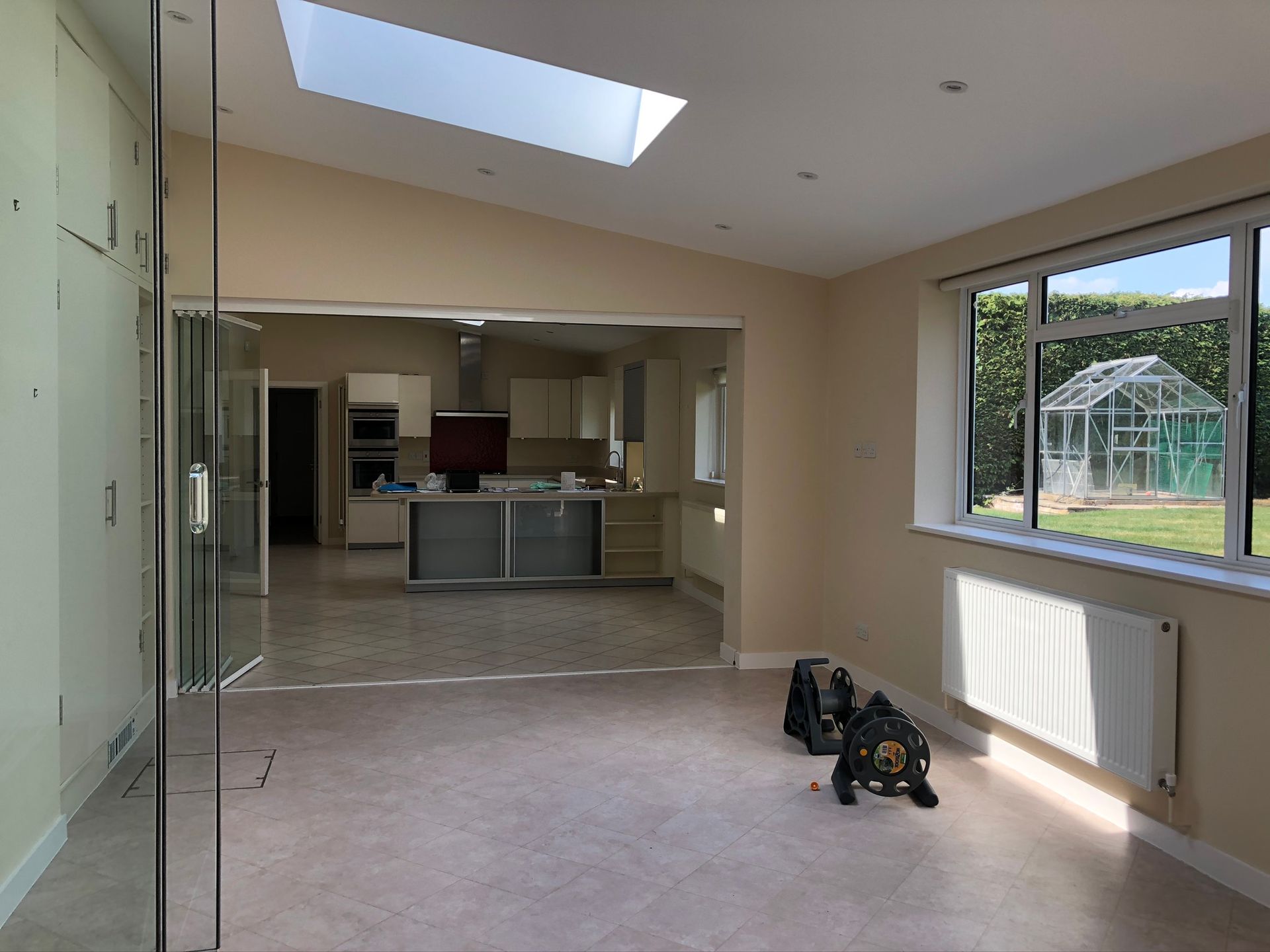 Empty modern room with large windows, skylight, and kitchen visible in the background