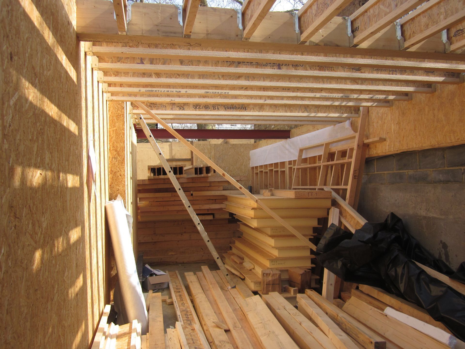 Partially built wooden room interior with stacked lumber, exposed beams, and construction materials.