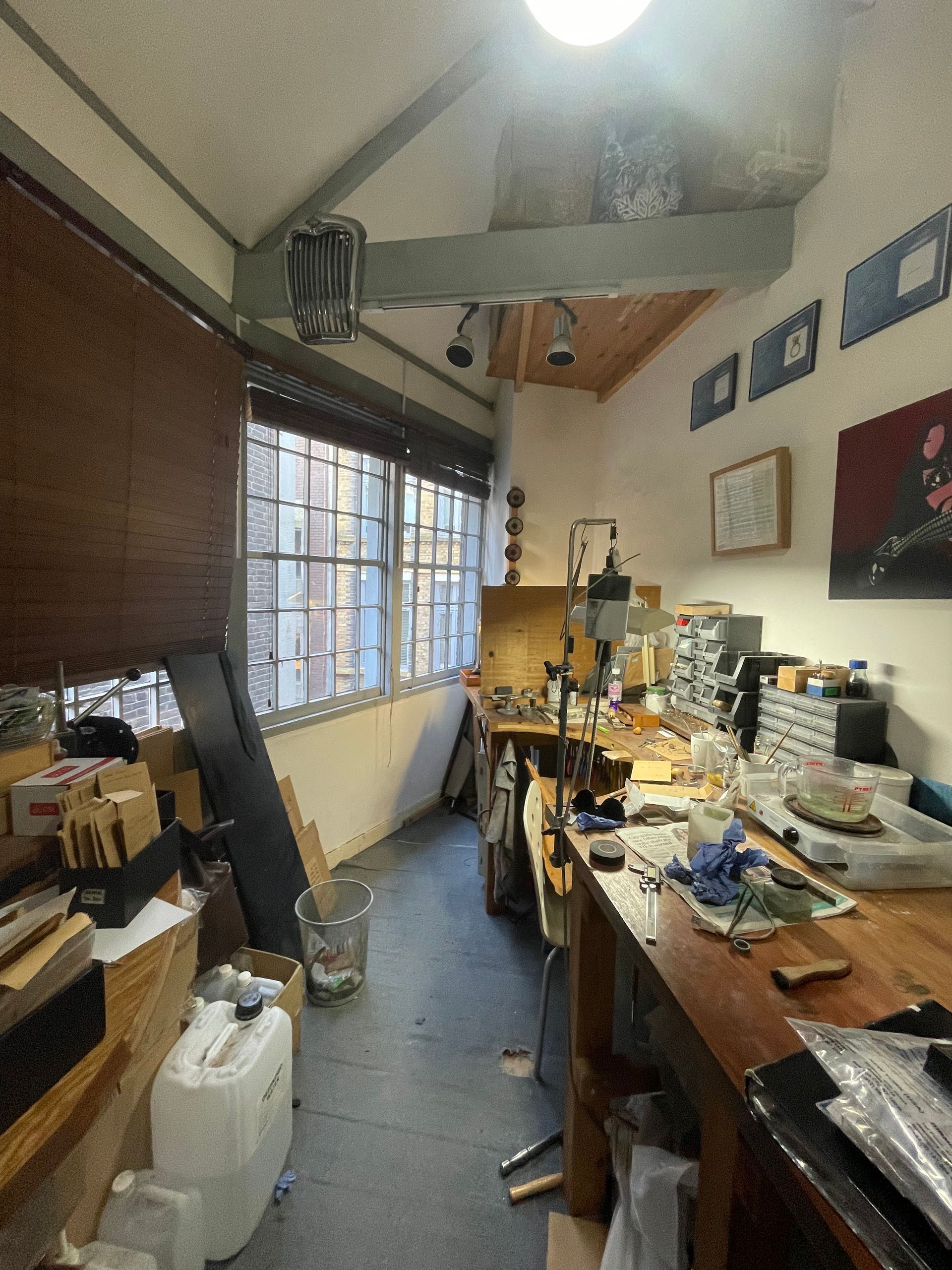 Cluttered workshop with workbenches, tools, and supplies under a slanted ceiling and window.