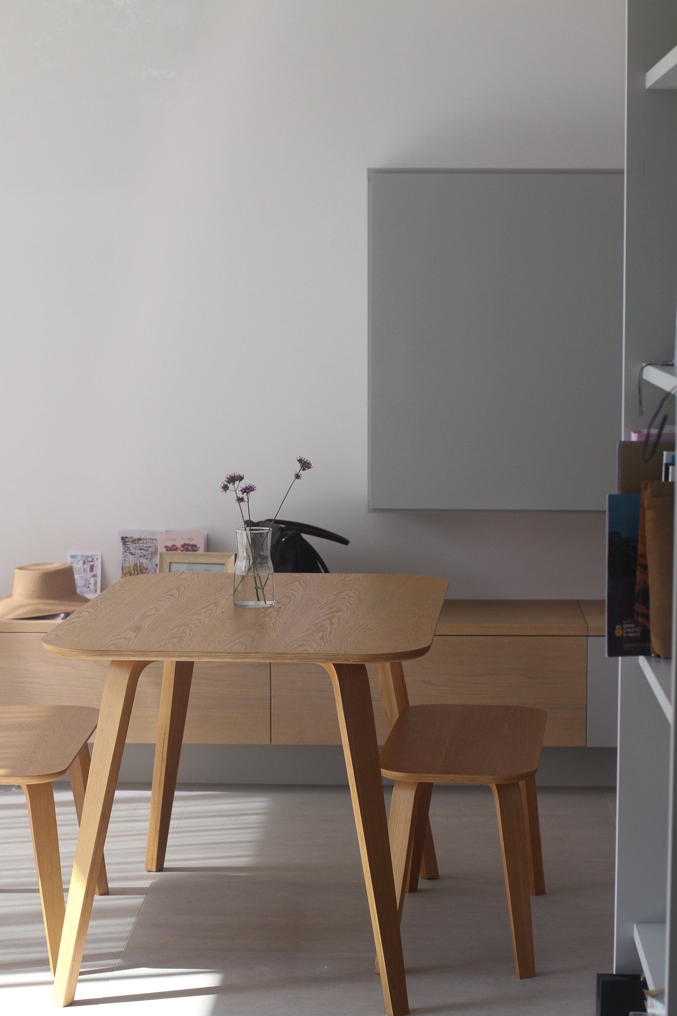 Wooden dining table and chairs in a minimalist room with a plain gray wall and soft light.