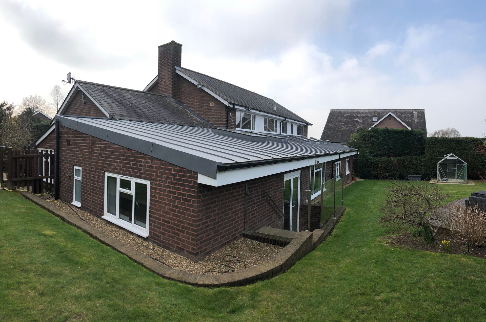 Brick house with gray roof and sunroom, seen from the backyard with a lawn and hedge.