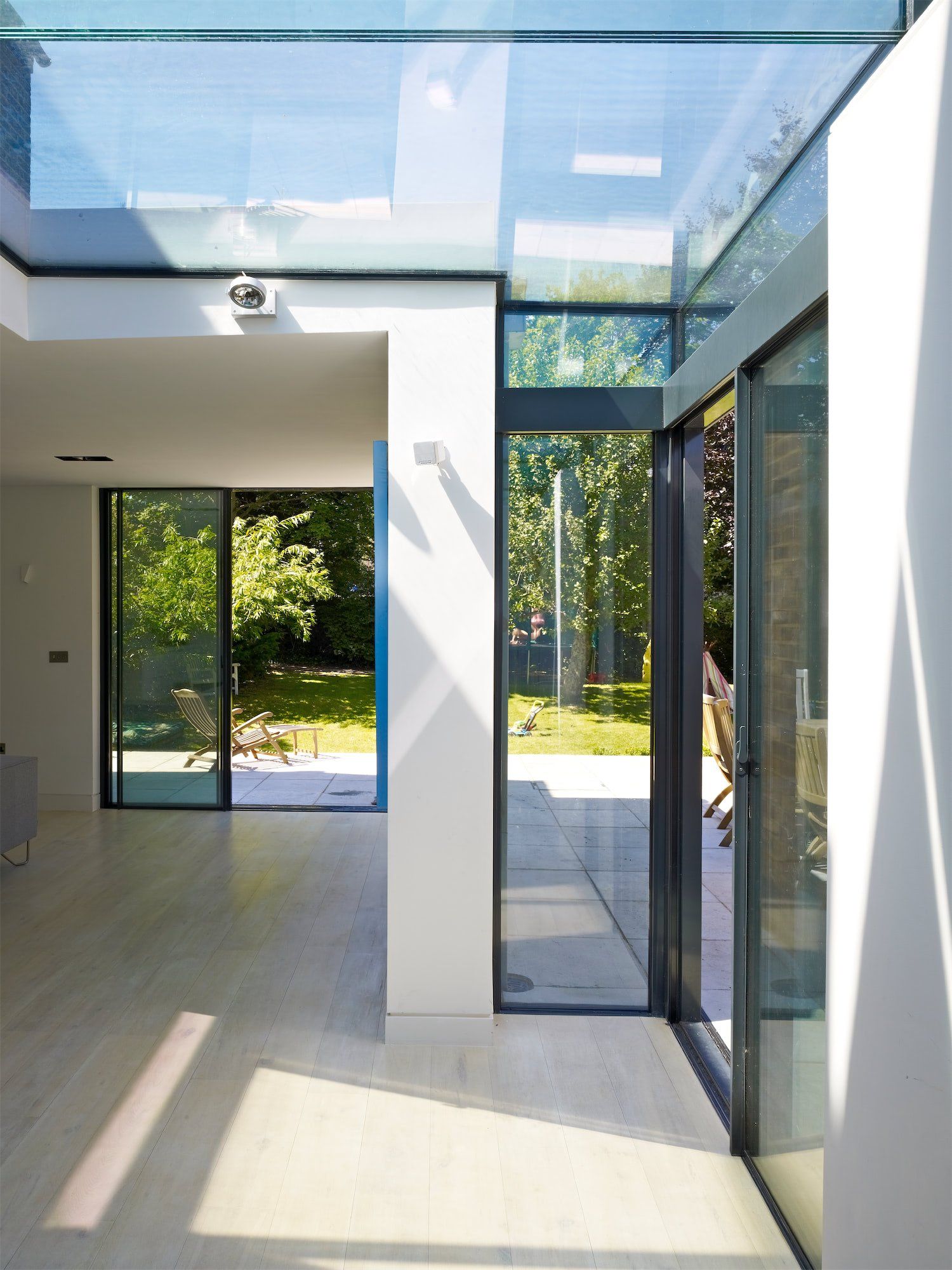 Bright modern room with glass doors, skylight, and sunlight on pale wood floors