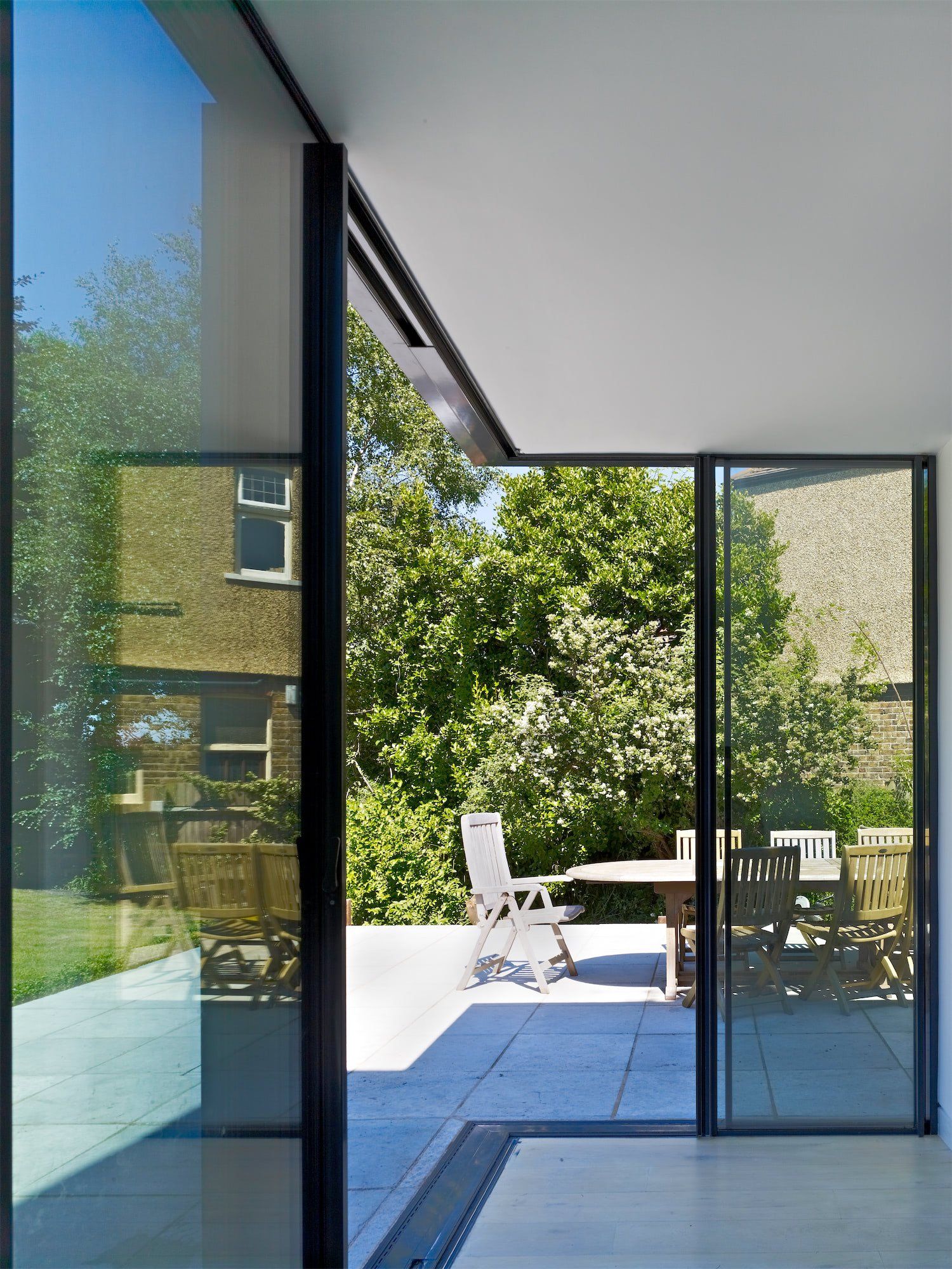Modern patio with glass doors, white chair and table, and trees outside in bright sunlight