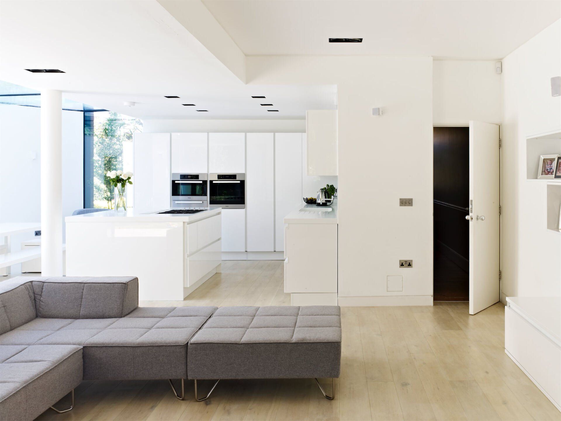 Modern white open-plan living room and kitchen with gray sectional sofa and light wood flooring