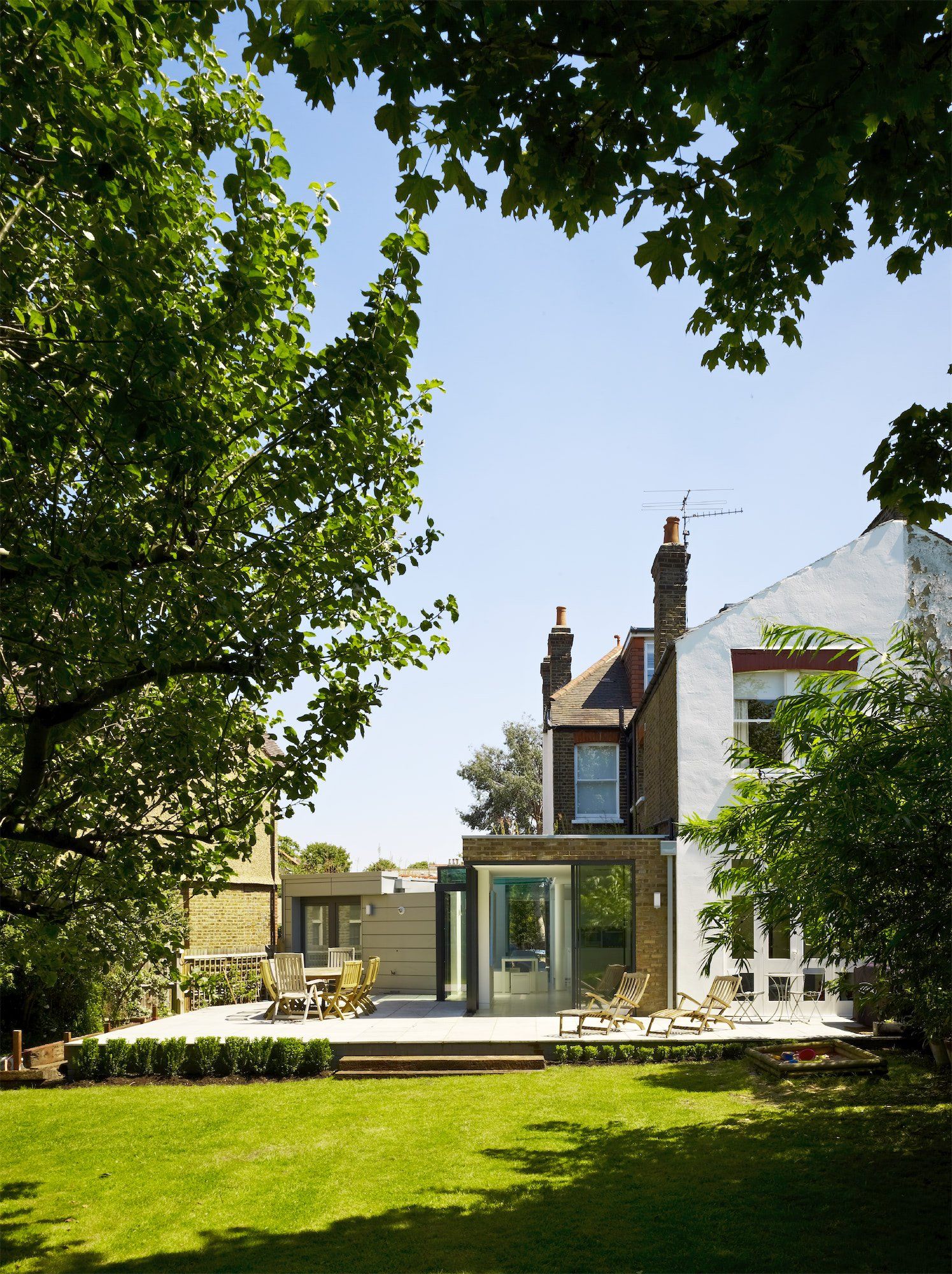 Stone house with glass patio, lush green lawn, and leafy trees framing a sunny backyard