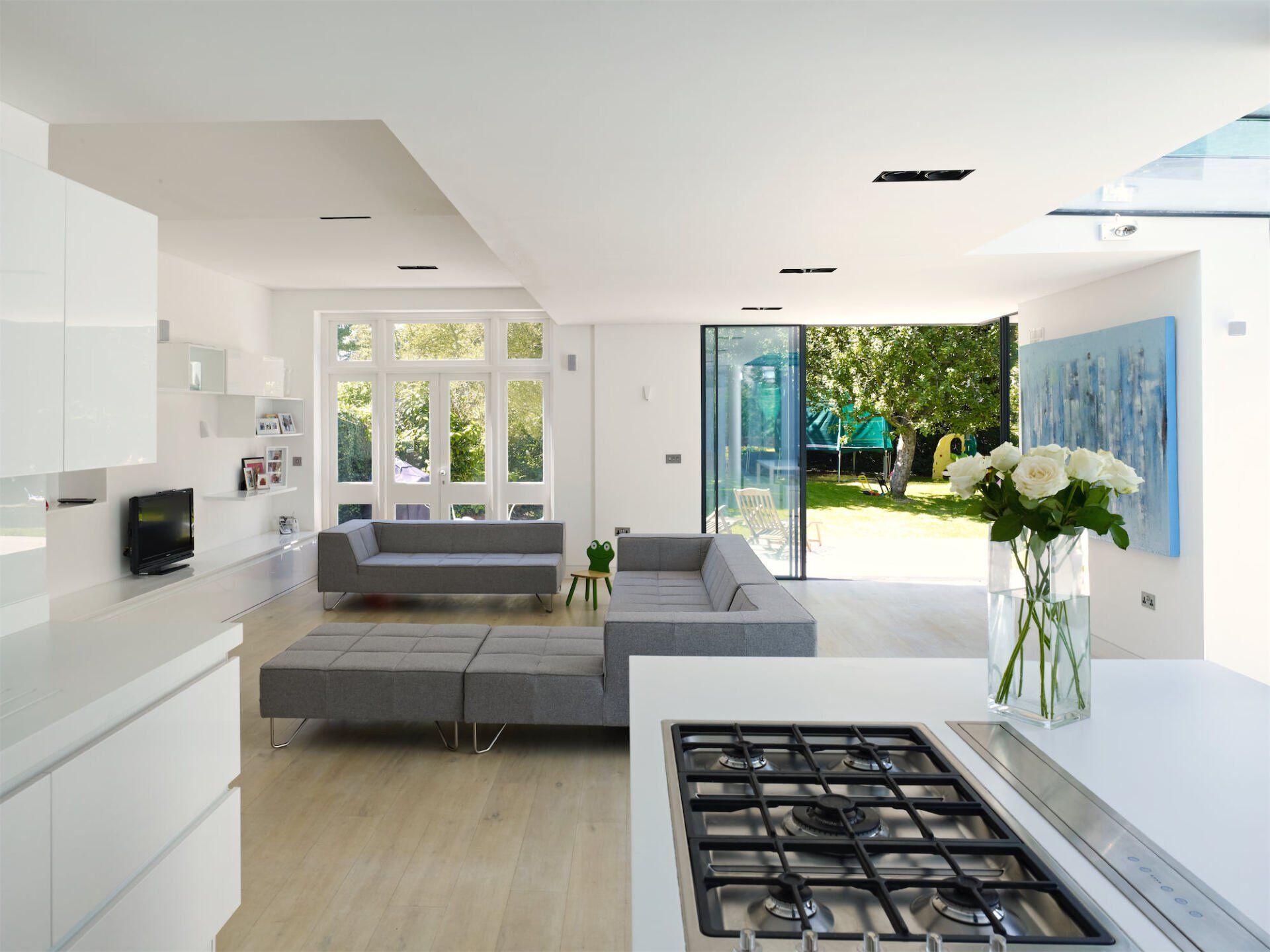 Modern white kitchen and living room with open glass doors to a sunny garden