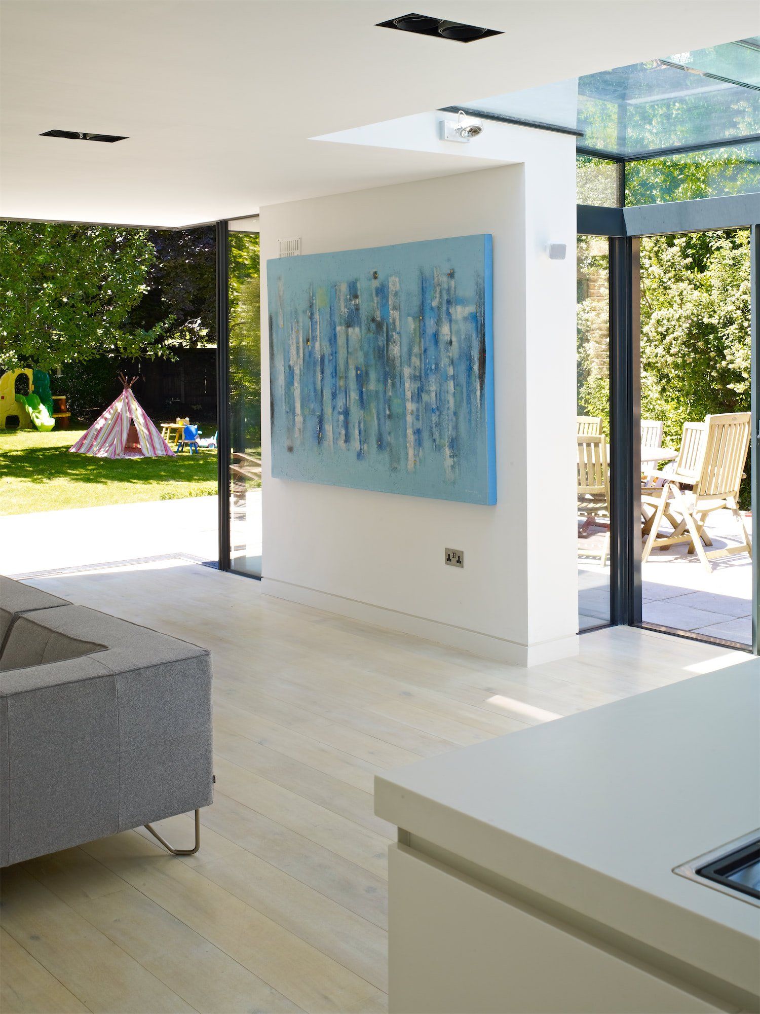Bright modern living room with open glass doors, abstract wall art, and a view of a sunny garden.