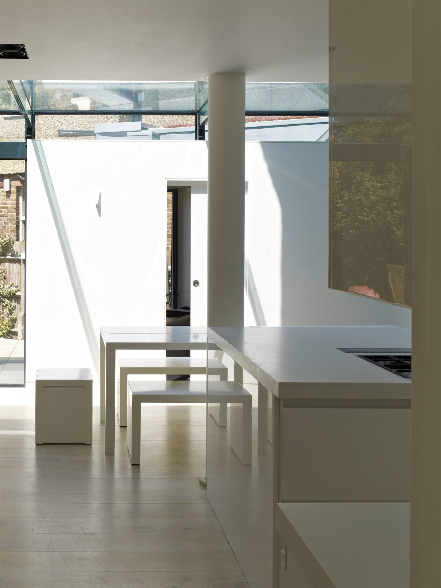Bright modern interior with white tables, stools, and sunlight streaming through large windows.