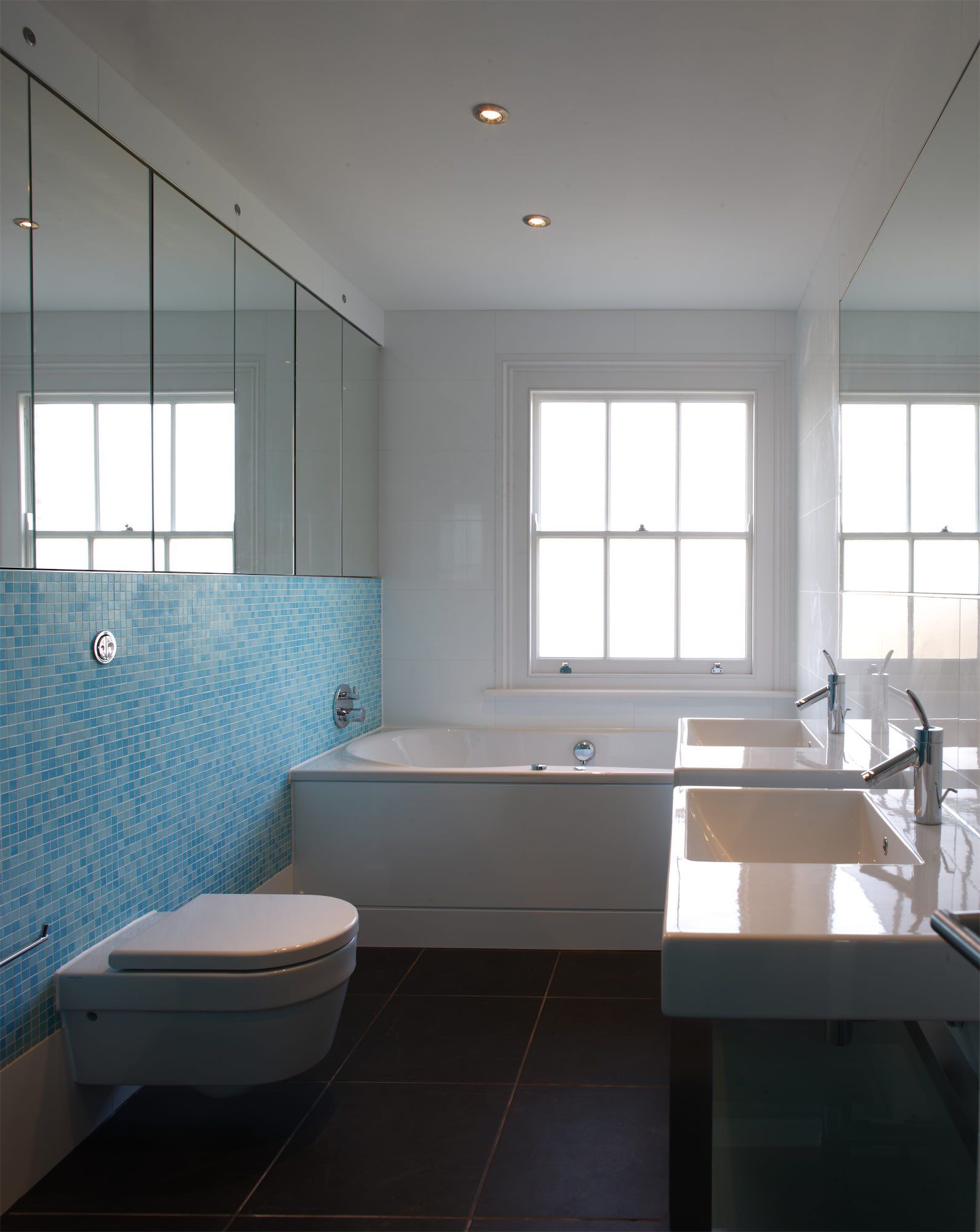 Modern bathroom with blue tile, white fixtures, and a window.