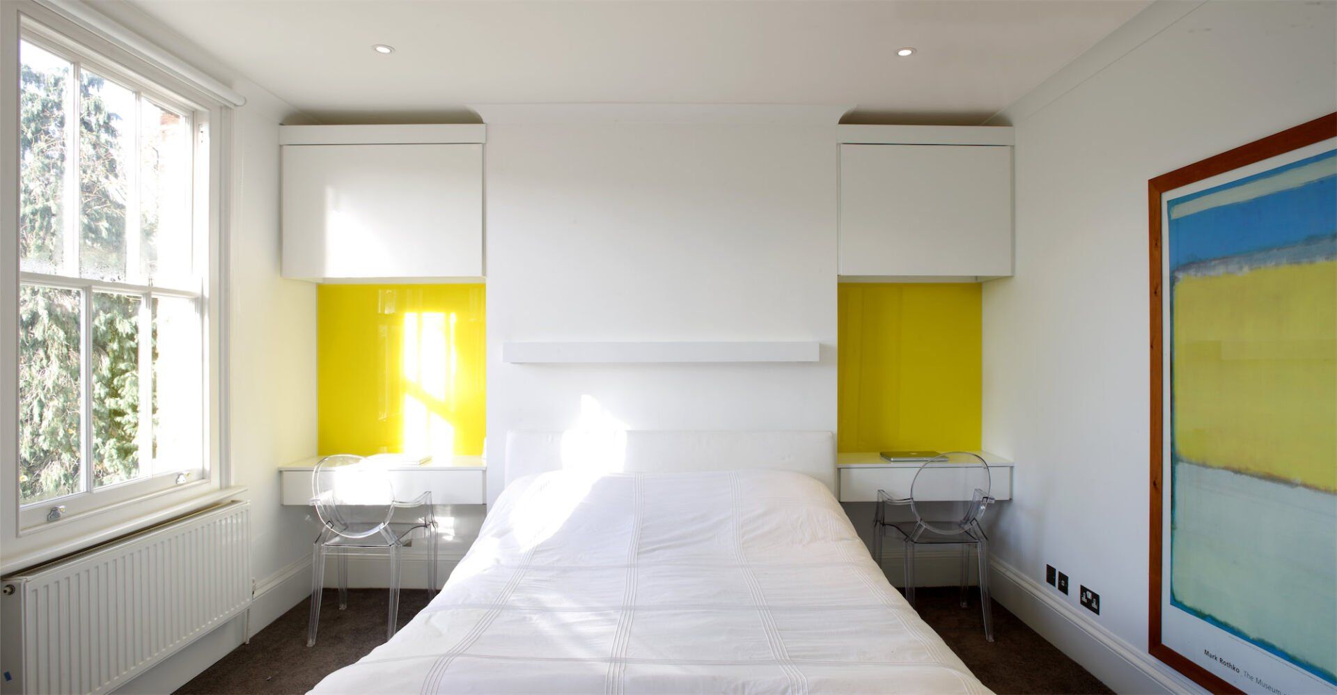 Bedroom with a white bed, yellow wall accents, white cabinets, a framed art piece, and a window.